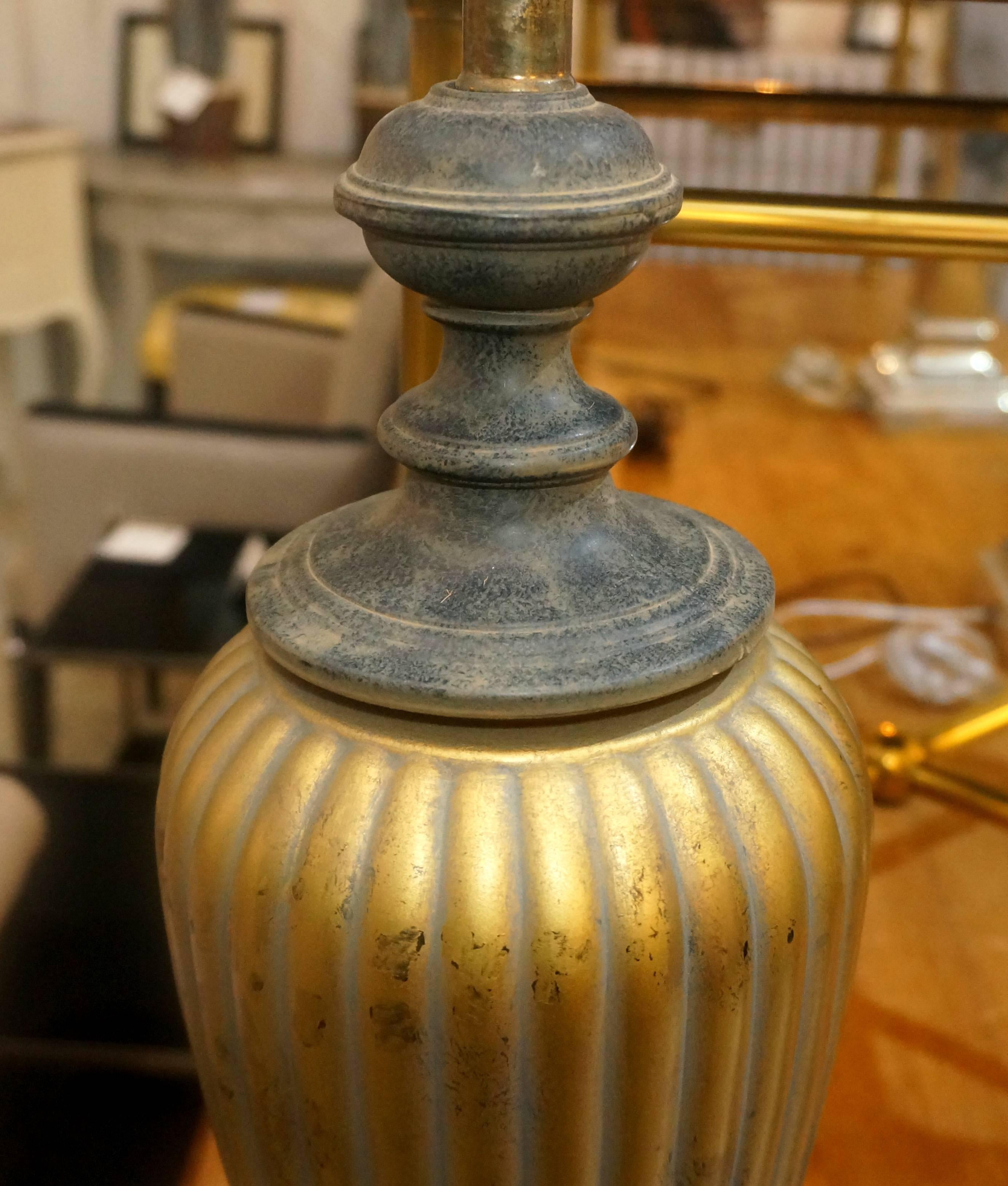 This handsome pair of Hollywood Regency style table lamps are metal and are finished in an antique gold and black coloration. The central form is ribbed which catches the light beautifully.

Note: Dimensions: 31.75" to top of finial.
