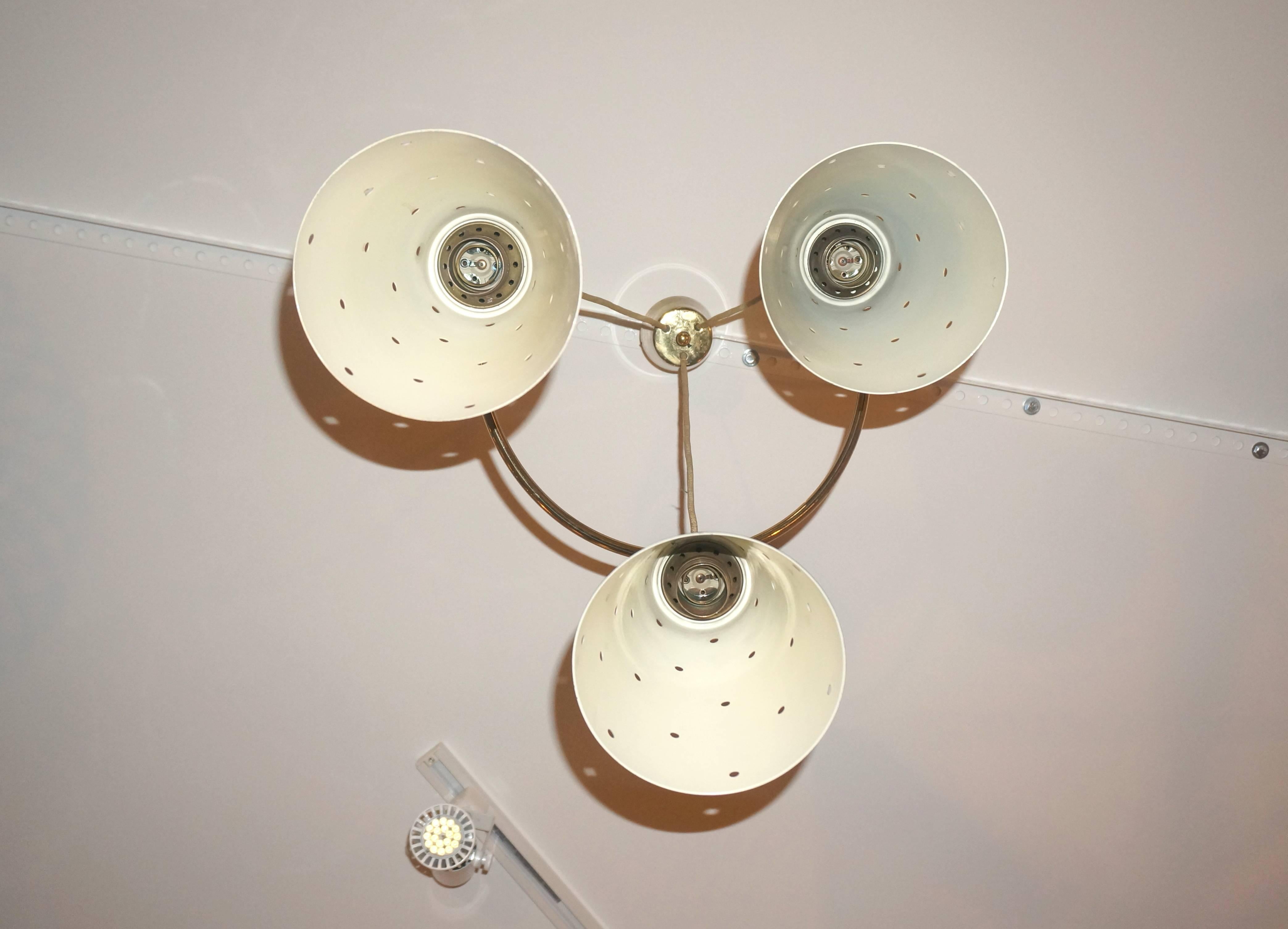 This Mid-Century Modern chandelier was produced in Italy in the 1950s. The three suspended metal shades are painted in enamel colors of burnt orange, black and cream. The hardware is polished brass and the electrical cords are wrapped in a
