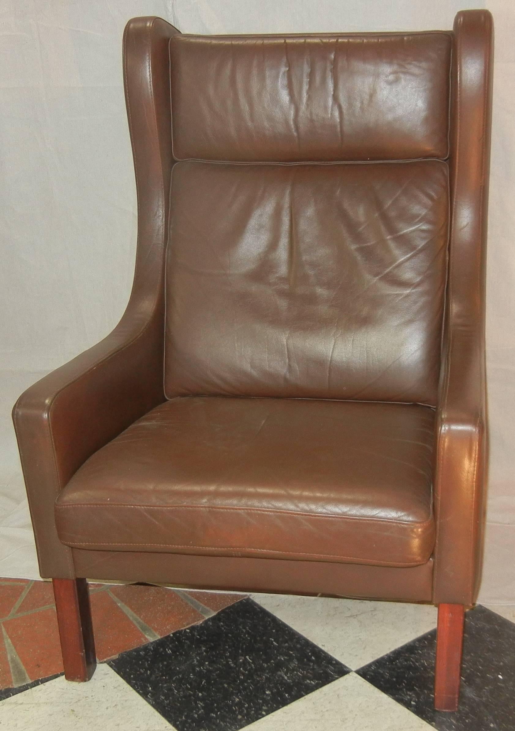 This leather wing chair has square dark teak legs, two loose cushions, and the original milk chocolate leather upholstery. It is all in good condition.

This design, after Børge Mogensen, is from the later part of his career when his goals of