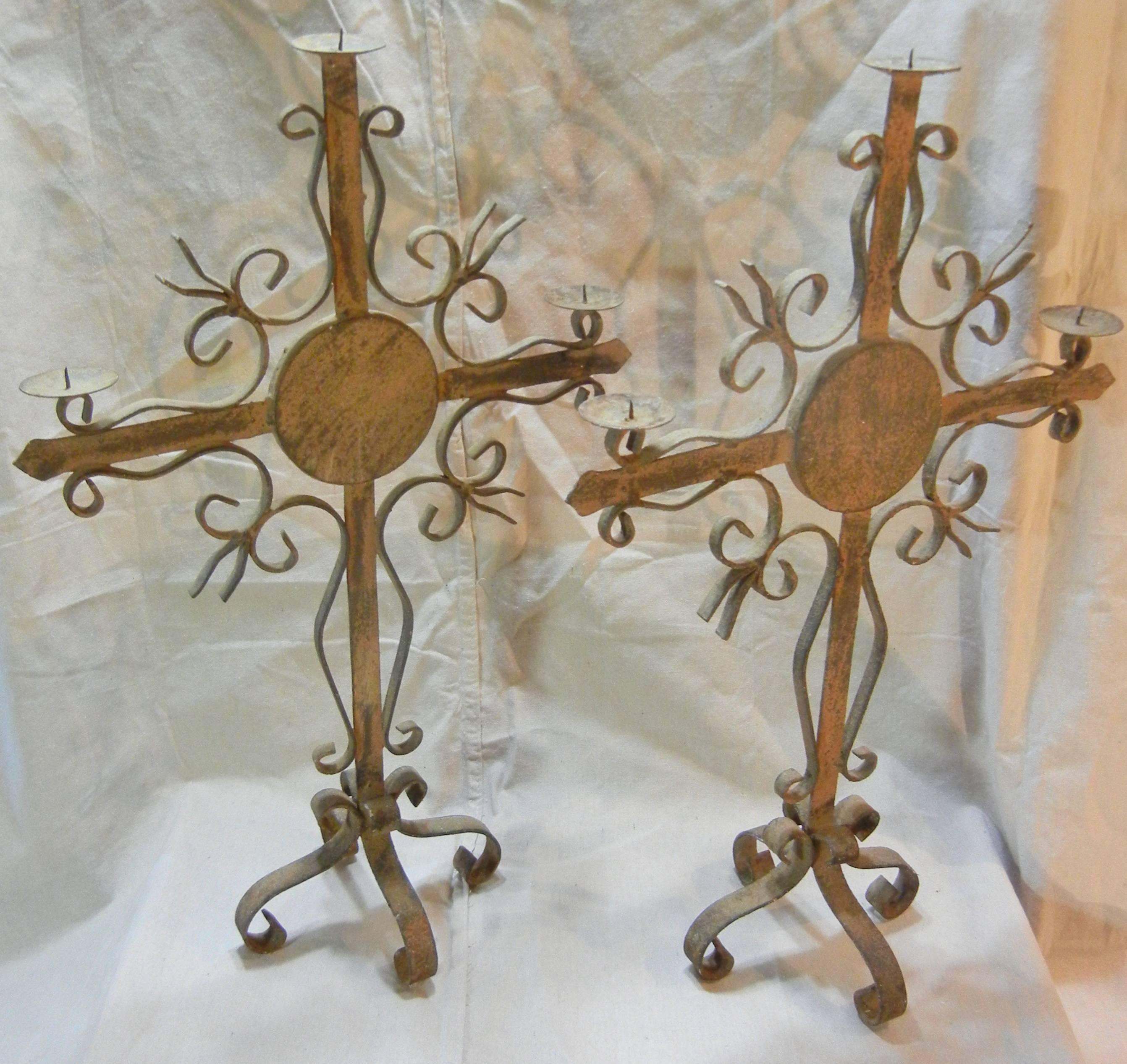 This pair of hand-wrought iron three-light candelabra have a rustic, weathered patina with remnants of taupe paint and they are in excellent condition. The shafts and cross-arms are accented with scrolls and spear points to form stylized