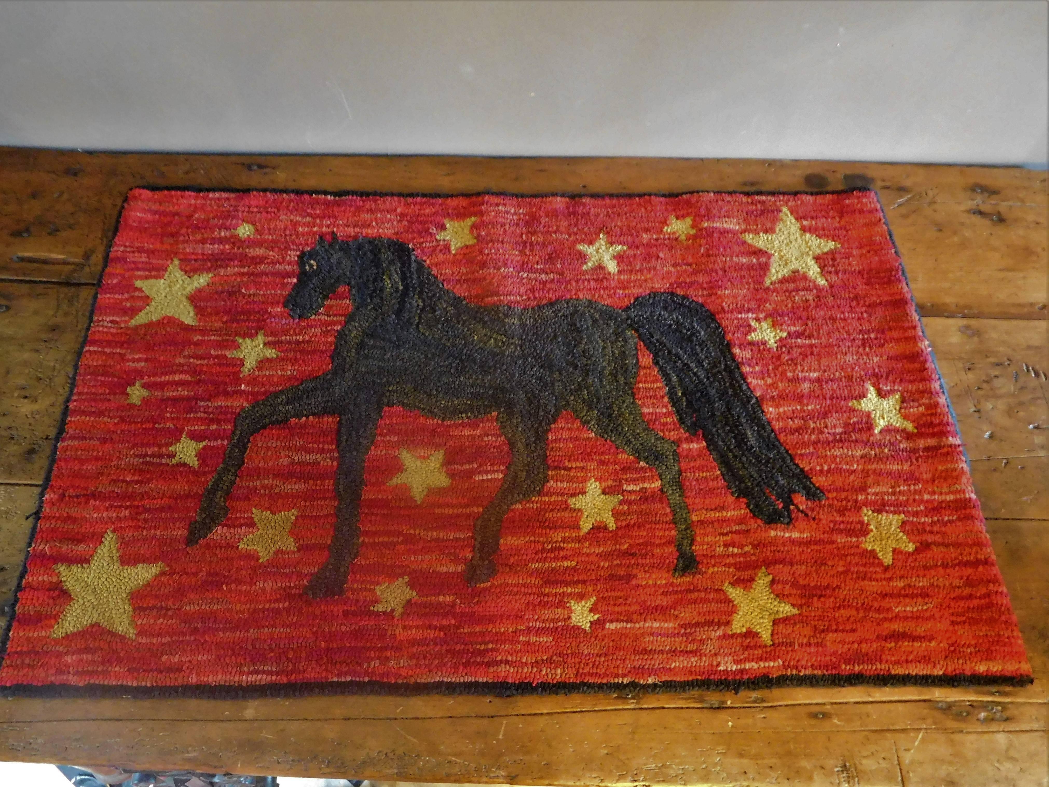 This hand-hooked hearth rug depicts a prancing black Morgan horse on a red field surrounded by gold stars, and outlined in black. The cotton and woollen rags are hooked onto an opened-up-burlap-bag foundation and backed by cotton tape around the