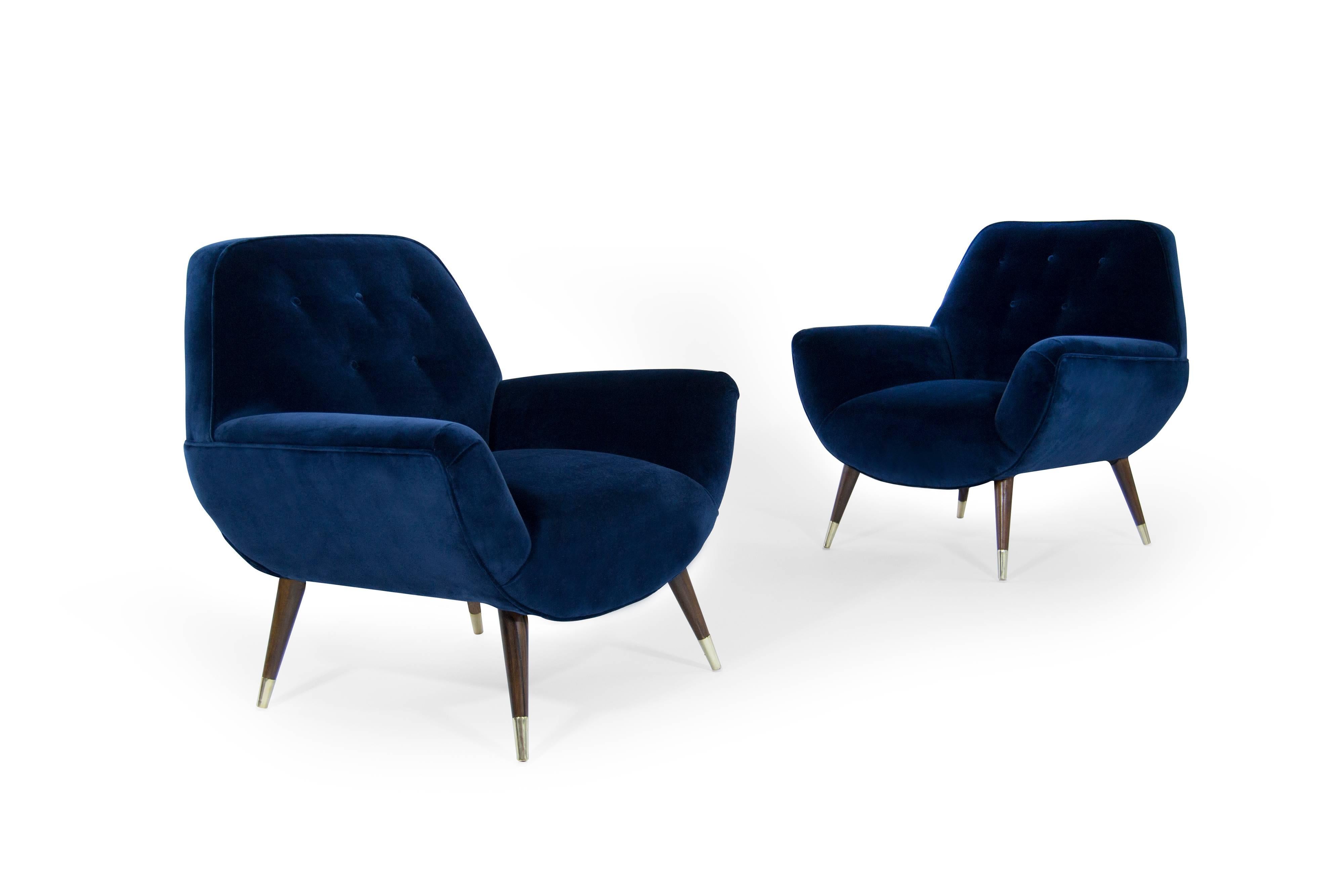 Stunning pair of lounge chairs featuring walnut splayed legs ending brass sabots. Newly upholstered in navy blue velvet. Legs fully restored, brass hand polished.