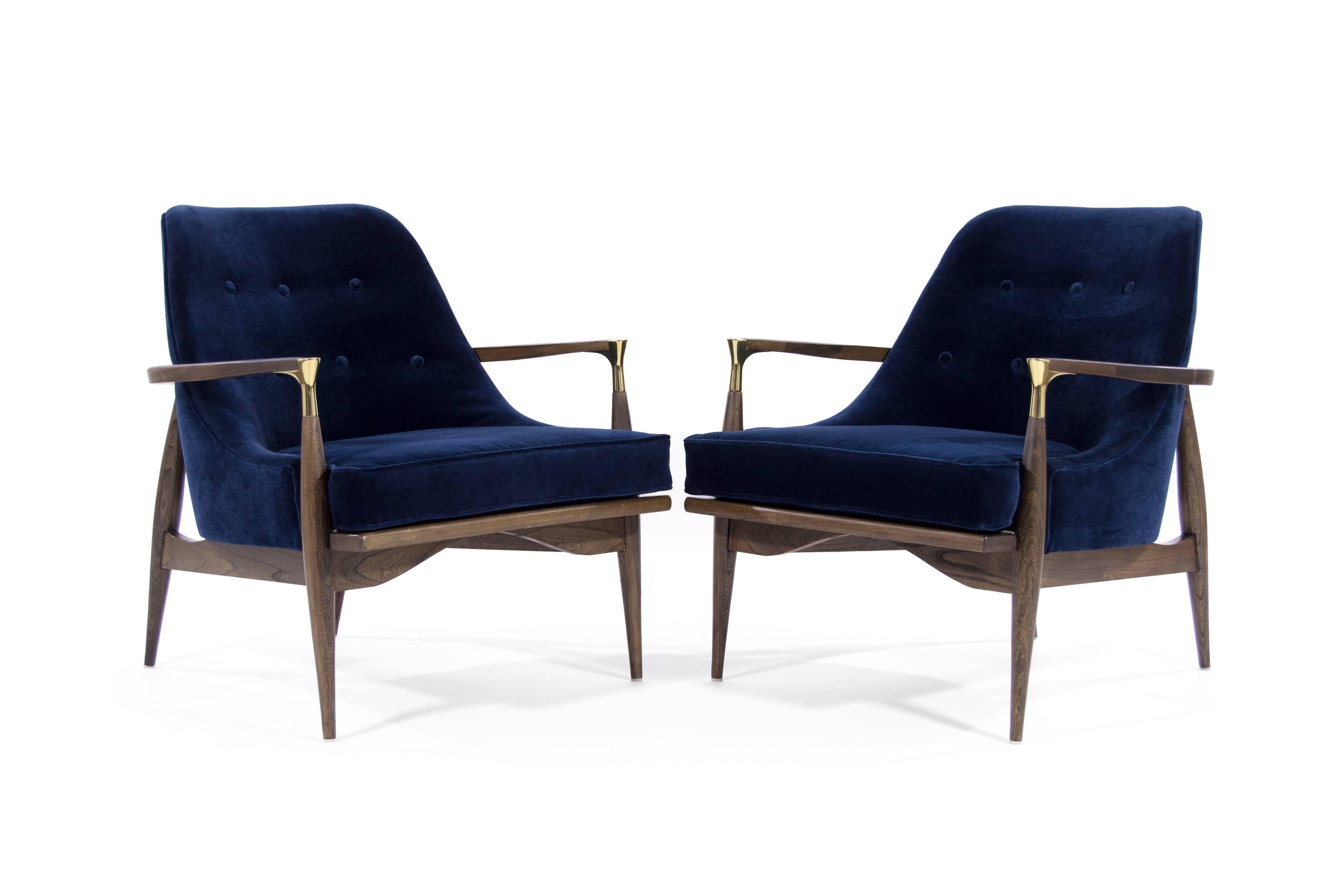 A rare pair of lounge chairs in the style of Ib Kofod-Larsen. Featuring brass details on arms. Newly upholstered in navy blue velvet, sculptural walnut frames completely restored.