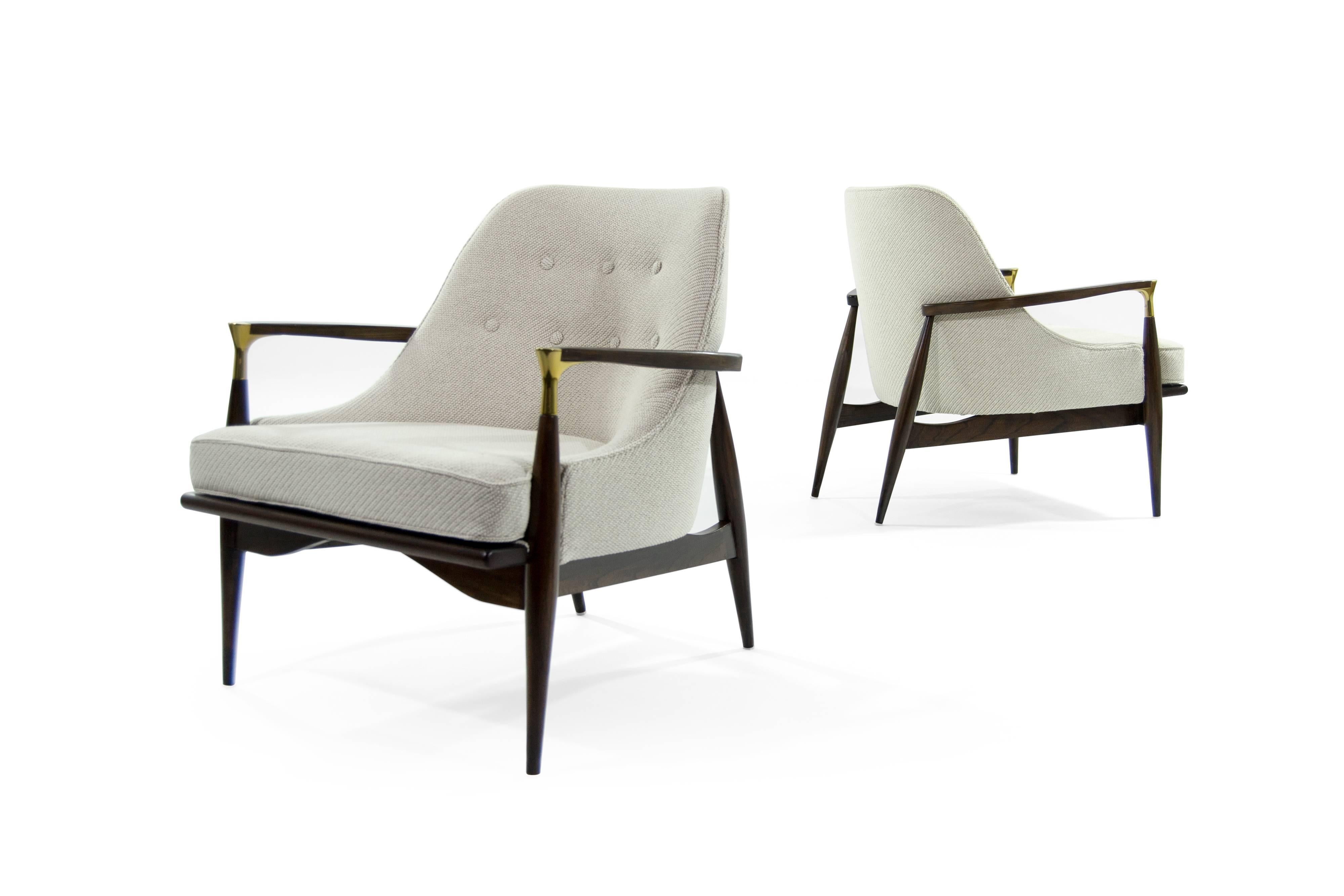 A rare pair of lounge chairs in the style of Ib Kofod-Larsen. Featuring brass details on arms. Newly upholstered in soft off-white Maharam/Kvadrat Coda soft wool. Sculptural walnut frames completely restored.