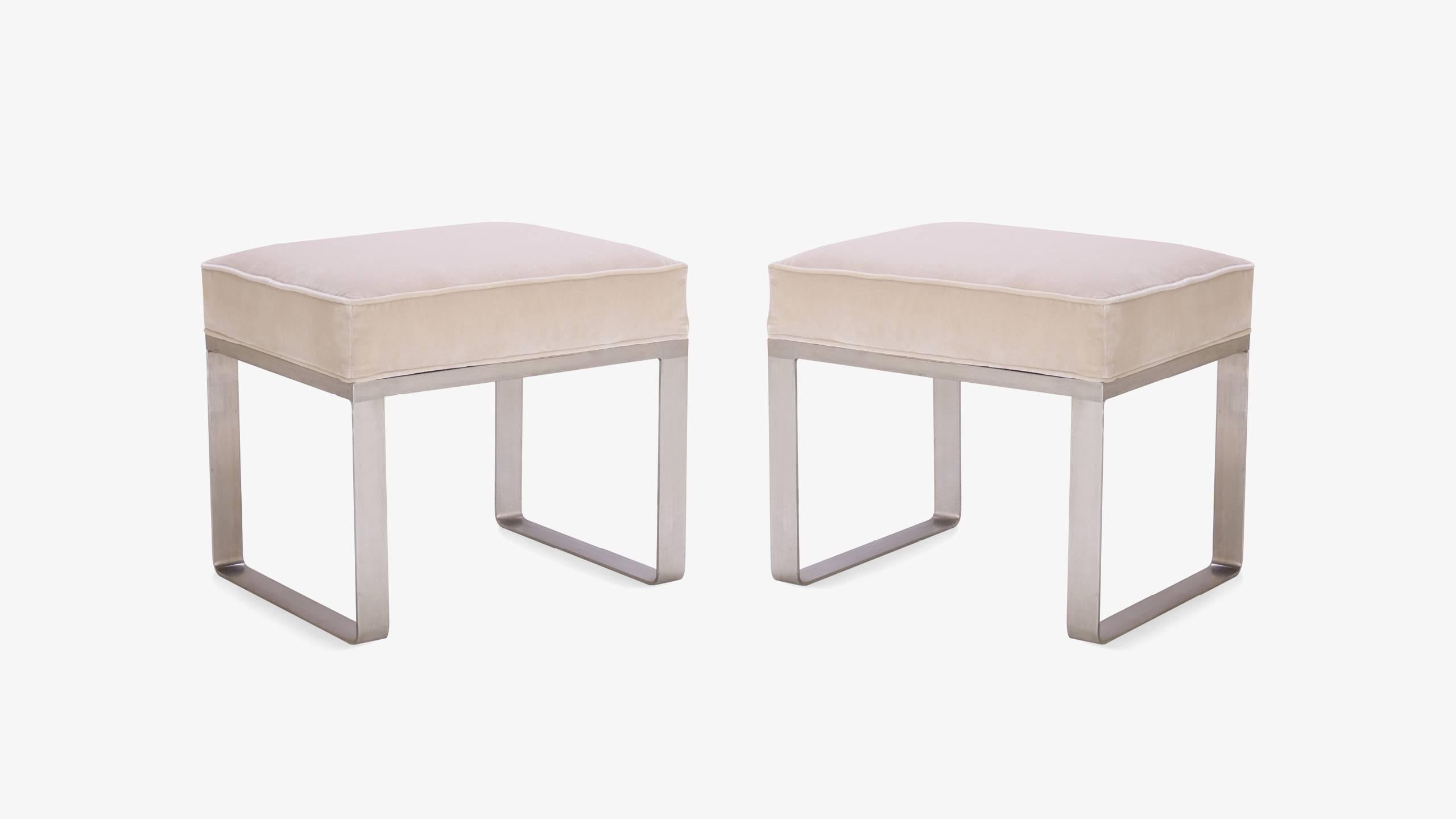 A pair of chic ottomans from the Ritz-Carlton hotel. The design exudes a minimalistic modernity with its brushed steel base. Perfect as a pair in a living space or at the foot of a bed, even as a single at a vanity. A generous cushion tops the base;