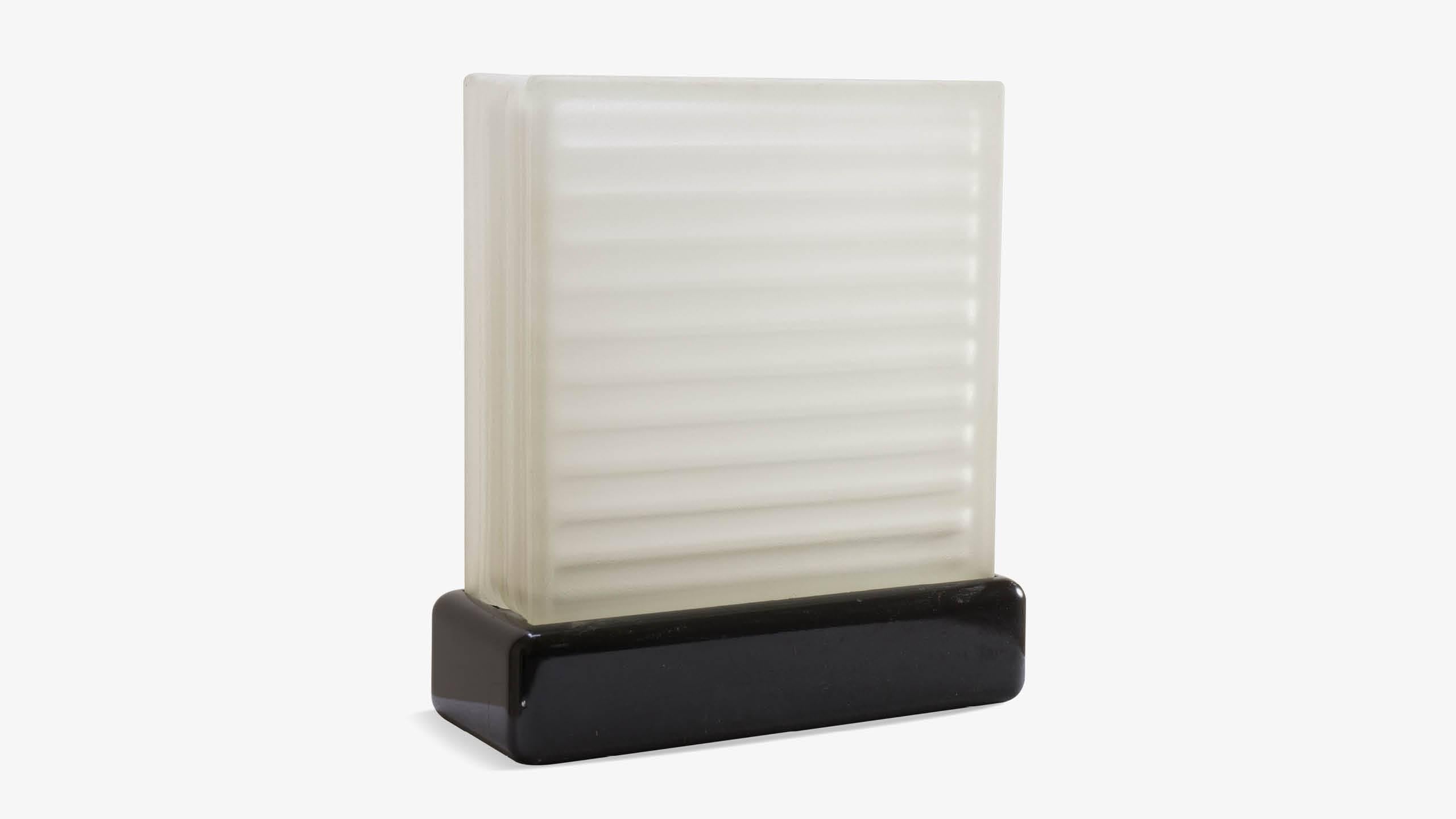 A functional piece of Art-Deco design, elegance and simplicity in one. A large frosted glass block sets inside a black base which cases a bulb. The glass block illuminates entirely delivering excellent accent lighting. Equipped with a sliding dimmer