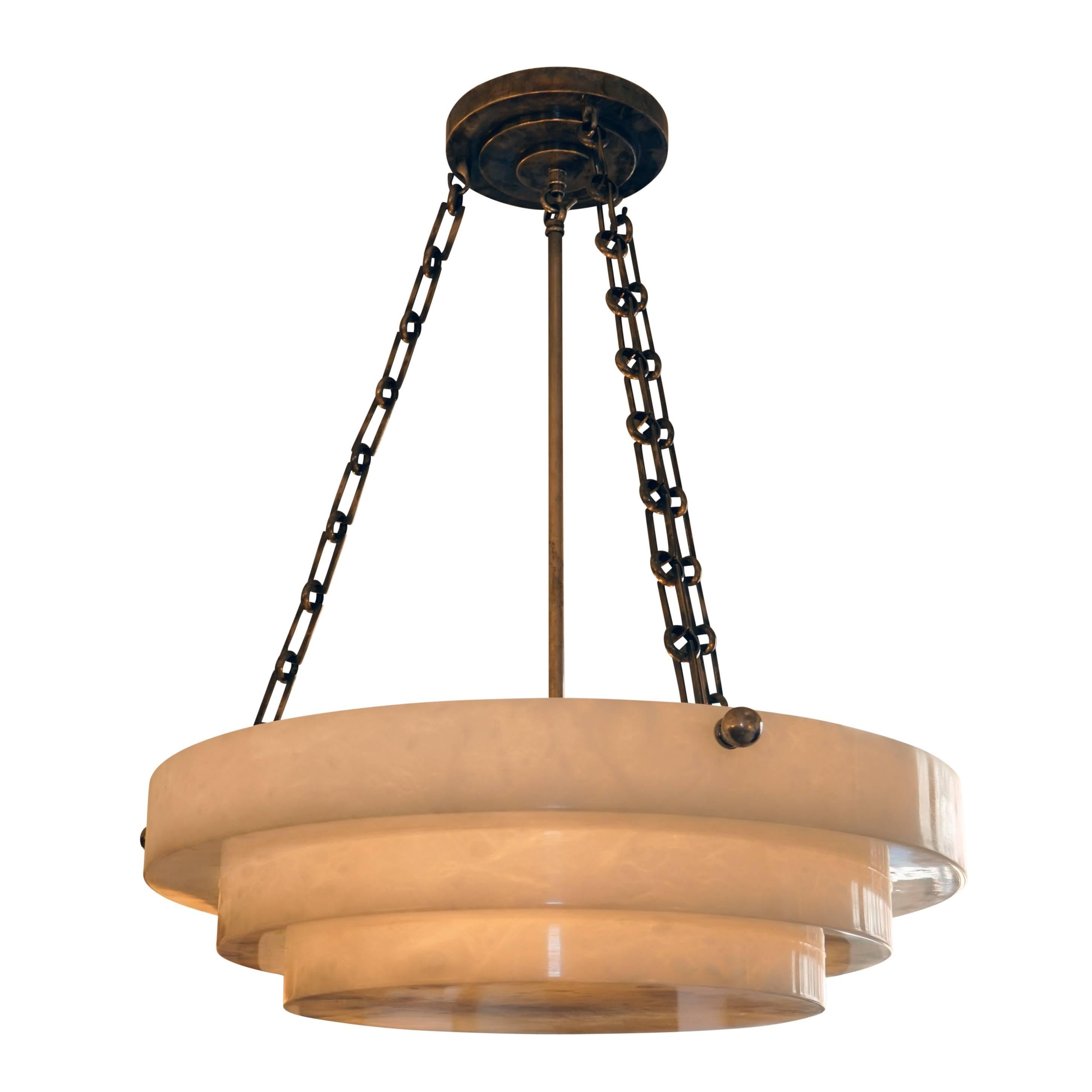 Carved from a single piece of white alabaster, the light features an Art Deco design, reminiscent of a three-tiered wedding cake. The pendant has recently been rewired on tarnished nickel chains and features a matching motif on the nickel canopy.