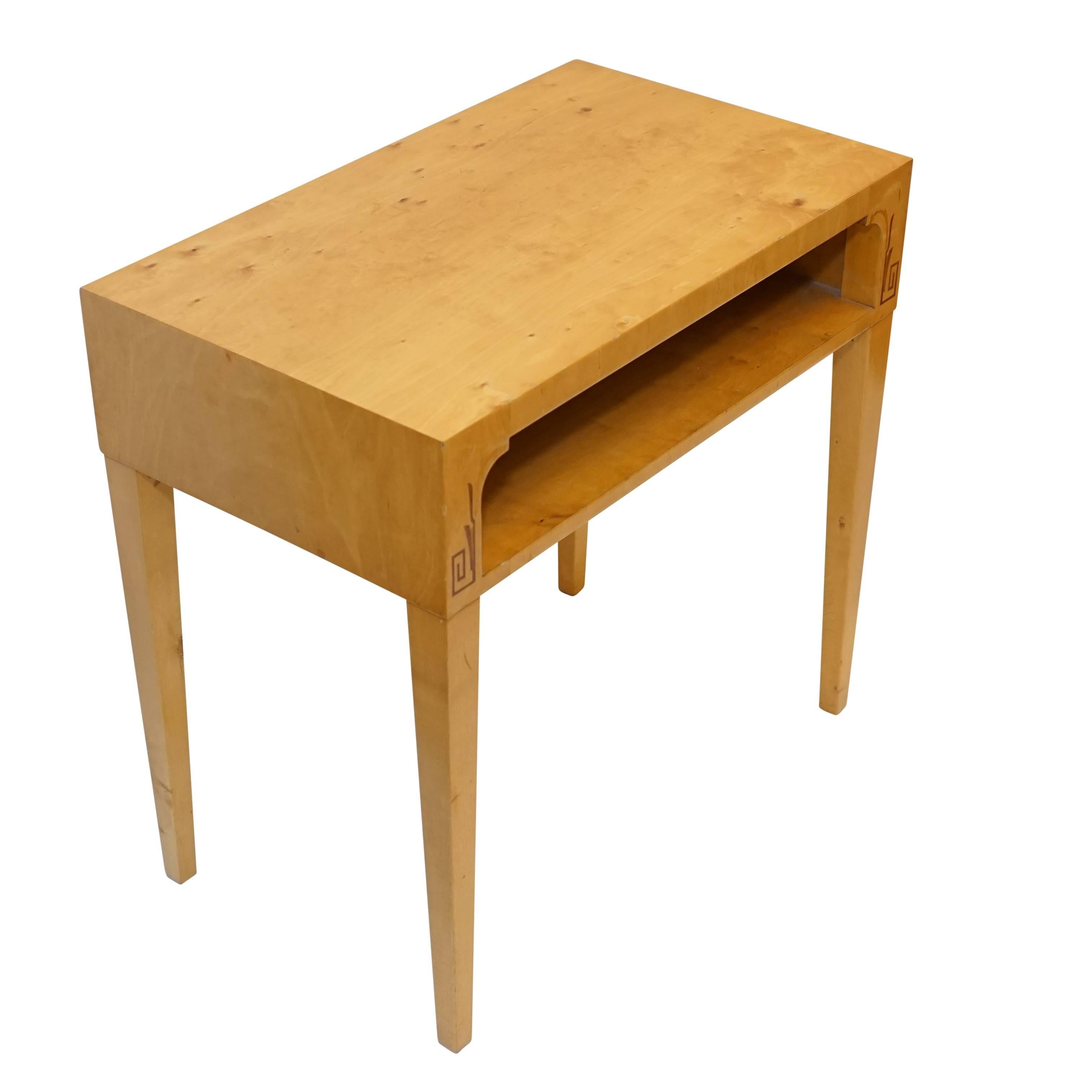 Crafted of solid birch and fir, the simple table features stylized intarsia of ash and mahogany flanking the lower open compartment which is veneered in finished golden birch.