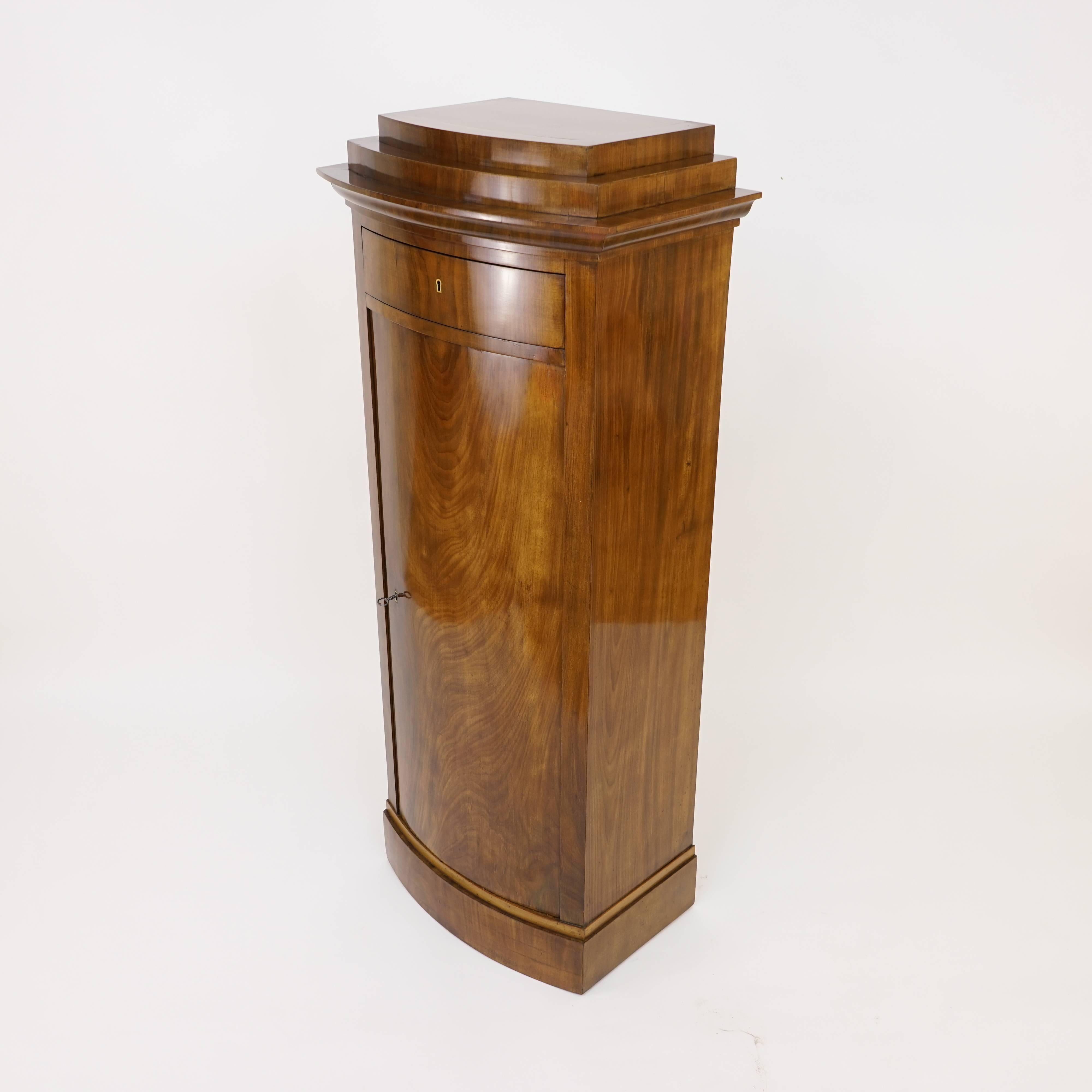 Constructed of solid birch, fir and mahogany and veneered in choice flame mahogany with birch banding, this Classic cabinet was often used as a pedestal, to display sculpture, a bust from antiquity or a reliquary. Beneath the locking drawer rest a