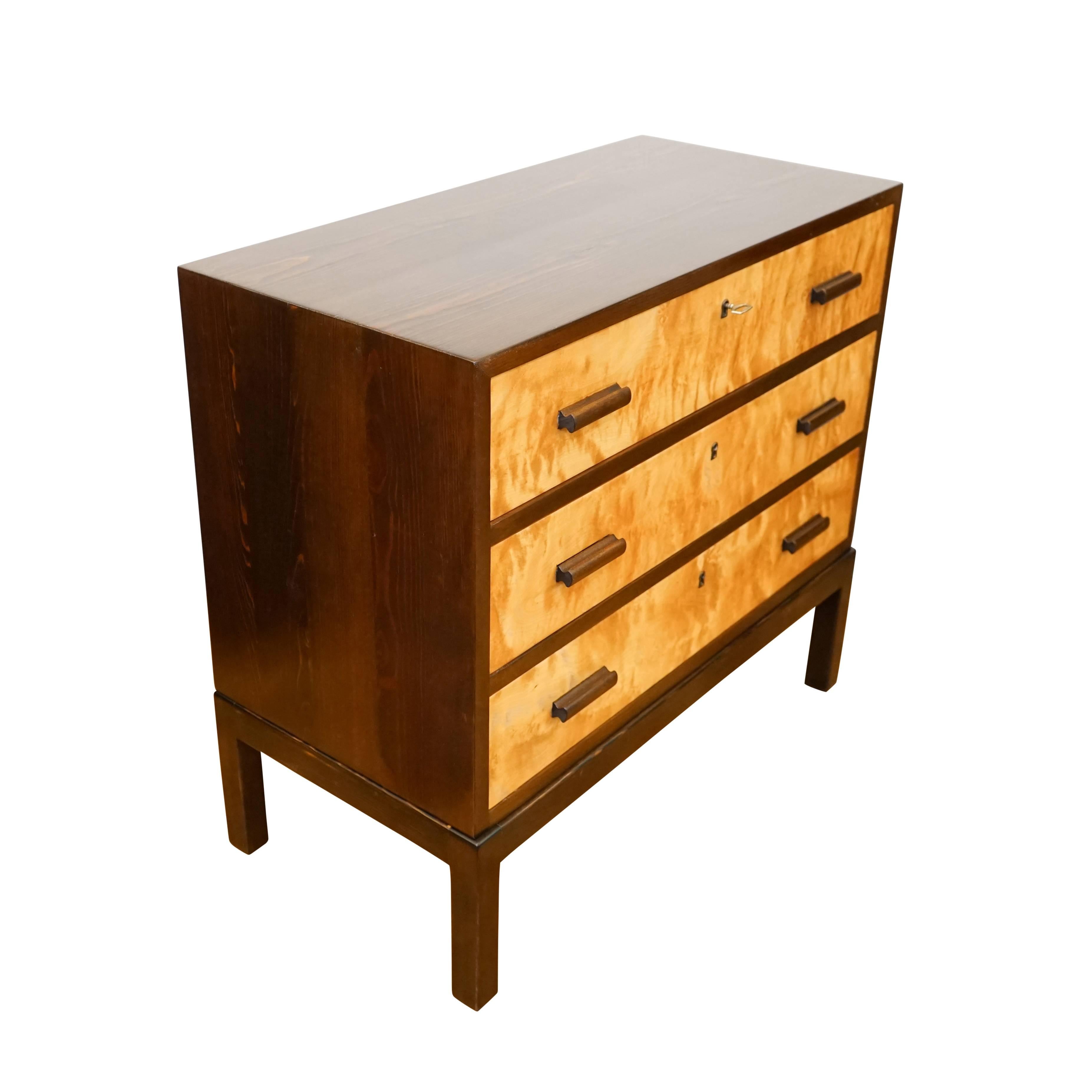 This Minimalist chest of drawers combines elegance with simplicity. Crafted of solid fir and birch veneers and stained golden birch and walnut tones, the locking three-drawer chest is useful in interiors featuring various types and tones of wood.