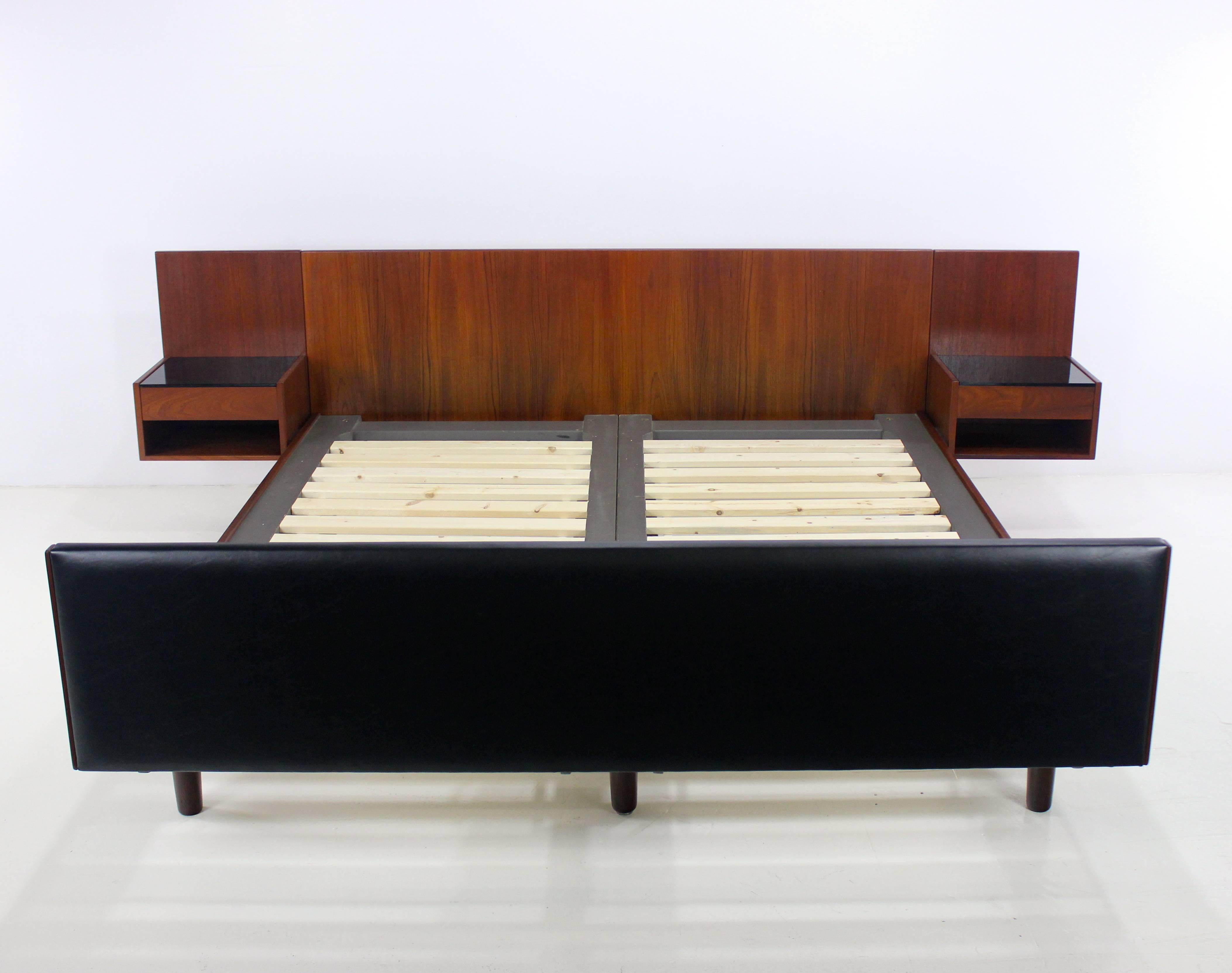 Exquisite Danish modern queen bed designed by Hans Wegner.
Getama, maker.
Rich teak with integrated, floating, black glass topped end tables featuring one drawer and cubby.
Black vinyl footboard.
Professionally restored and refinished by