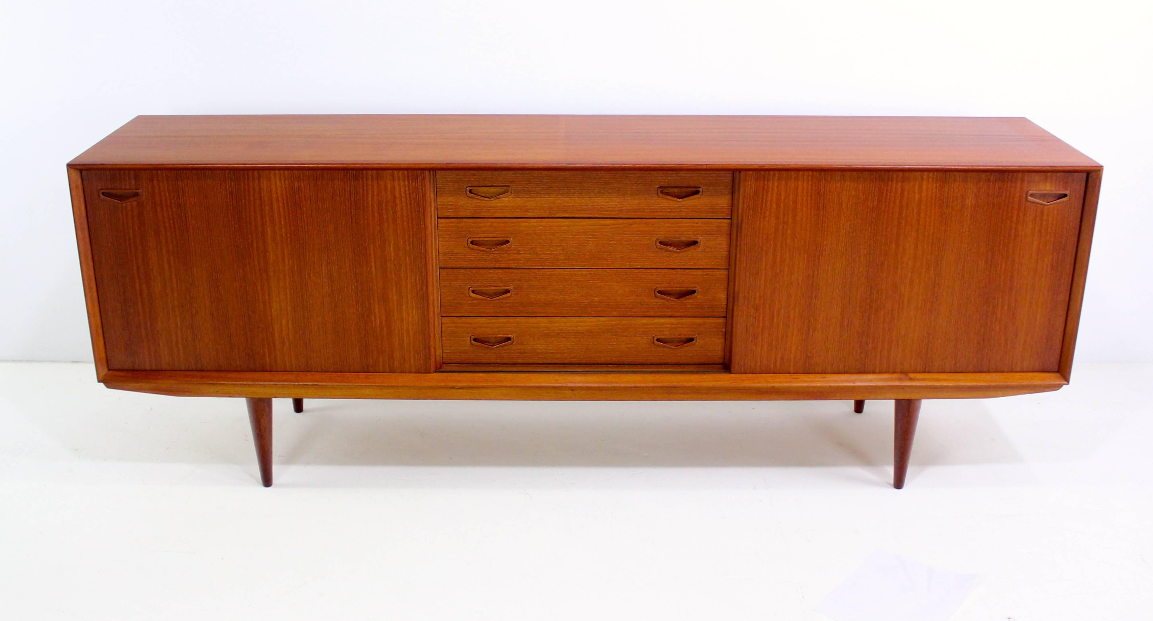 Danish modern credenza with timeless modern style.
Clausen & Søn, maker.
Richly grained teak.
Four drawers with chevron handles in the middle, the top drawer is felt-lined.
Sliding doors open to adjustable shelving on each end.
Finished on the