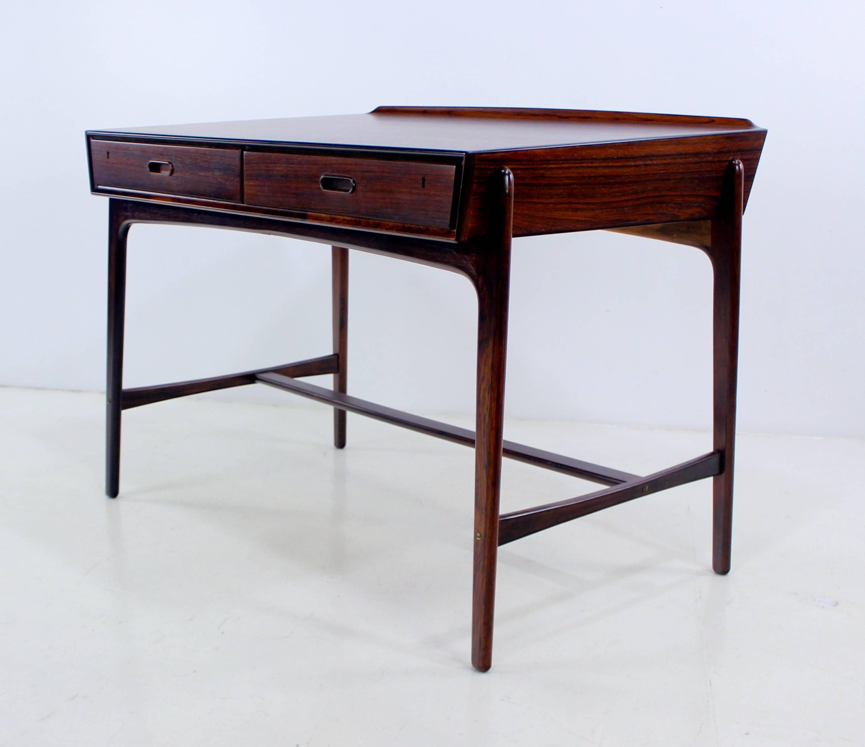 Distinctive Danish modern desk designed by Svend Madsen.
Rare elegance and élan.
Rich rosewood.
Two locking drawers (key included).
Sculptural base and lip on back edge.
Professionally restored and refinished by LookModern.
Matchless quality