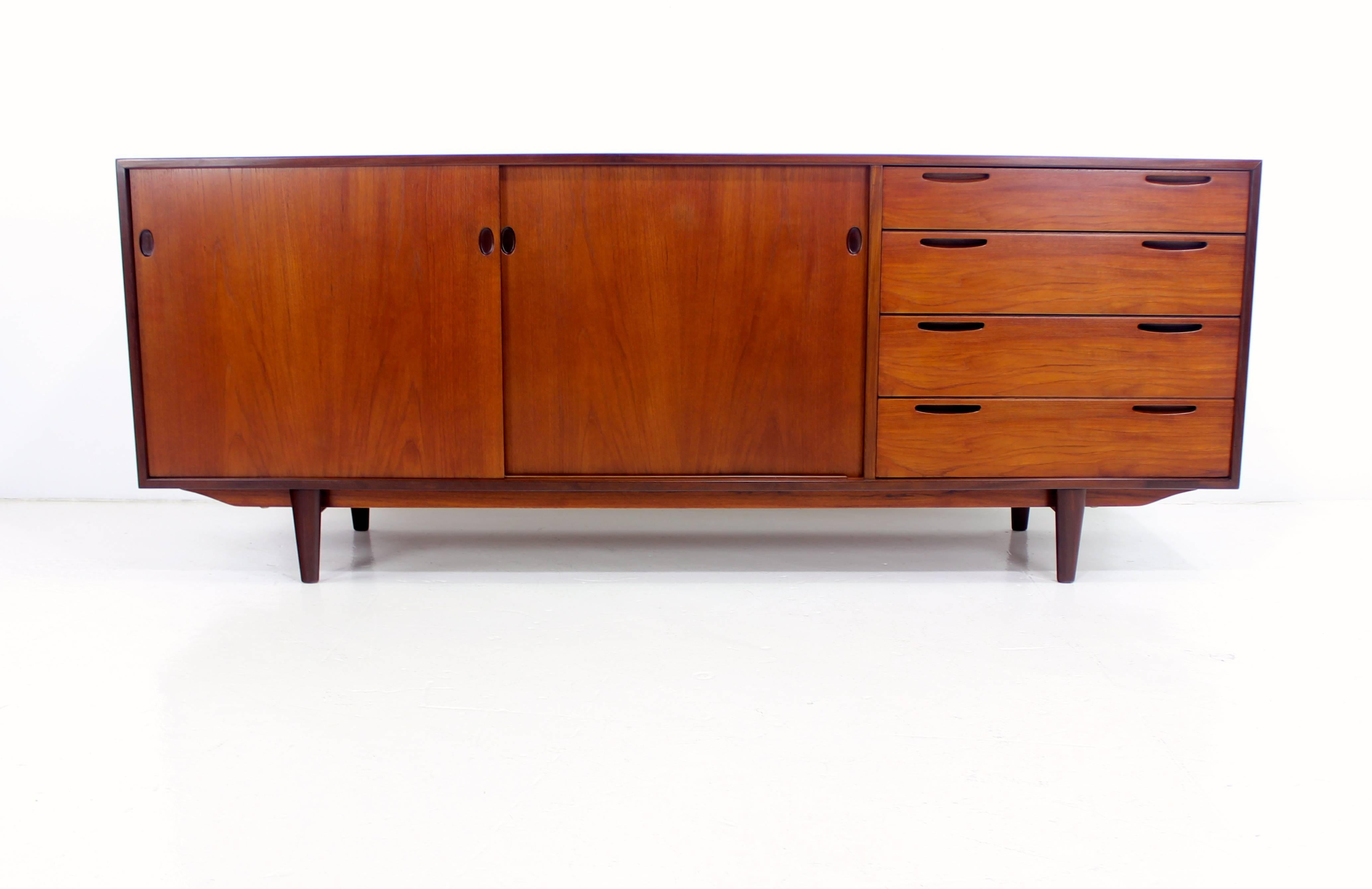 Danish modern credenza designed by Ib Kofod-Larsen.
Richly grained teak with beautifully crafted base.
Sliding doors open to two drawers in the middle, adjustable shelf on the left. 
Four generous drawers with exquisitely designed inset pulls on