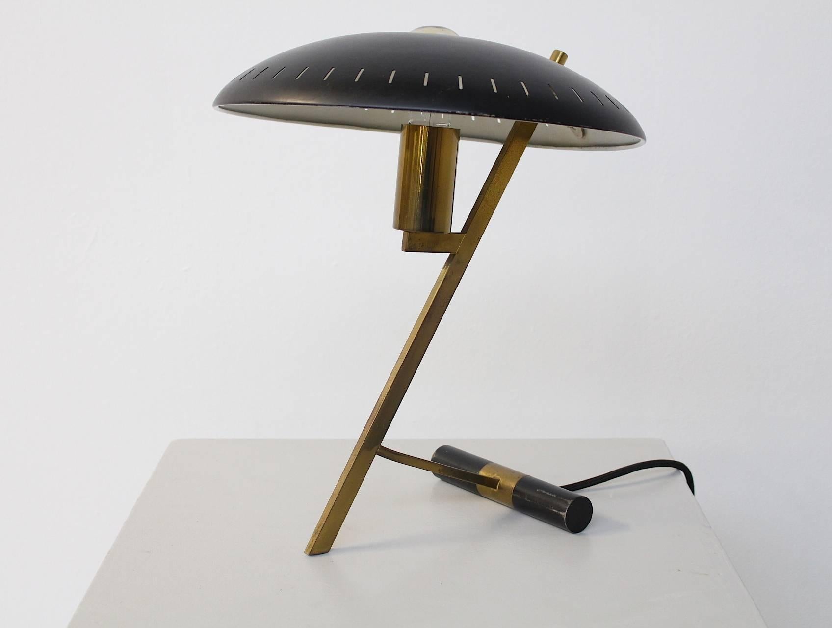 An iconic Dutch-industrial desk or table lamp designed by designer and architect Louis Kalff; for the Philips Company, Holland, 1955. This is the first edition with a brass frame and the black disk-shaped perforated black lacquered shade. The shade