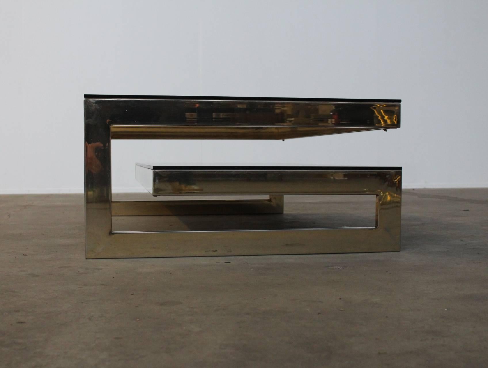 Stunning architectual two-tiered rectangular gold plated 23ct coffee table attributed to Maison Jansen, circa 1970. A very eye-catching minimalist design. On the bottom level a smoked mirror and on the upper level a dark smoked glass top. The frame