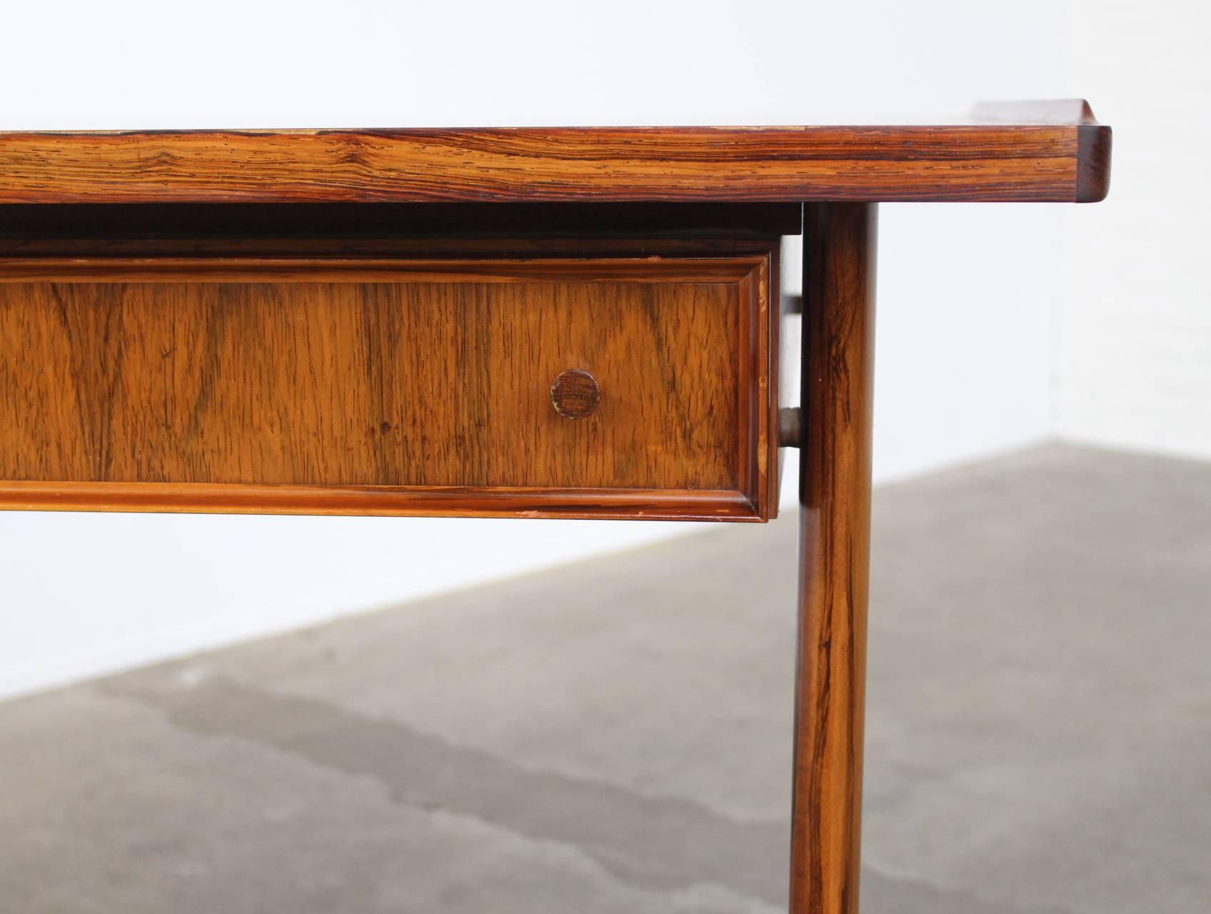 Very elegant rosewood writing desk in the manner of Arne Vodder with two asymetrical drawers that hang below the desk top. The wood used is a beautiful flaming Brazilian rosewood and it has some nice details like the upstanding edges on the sides