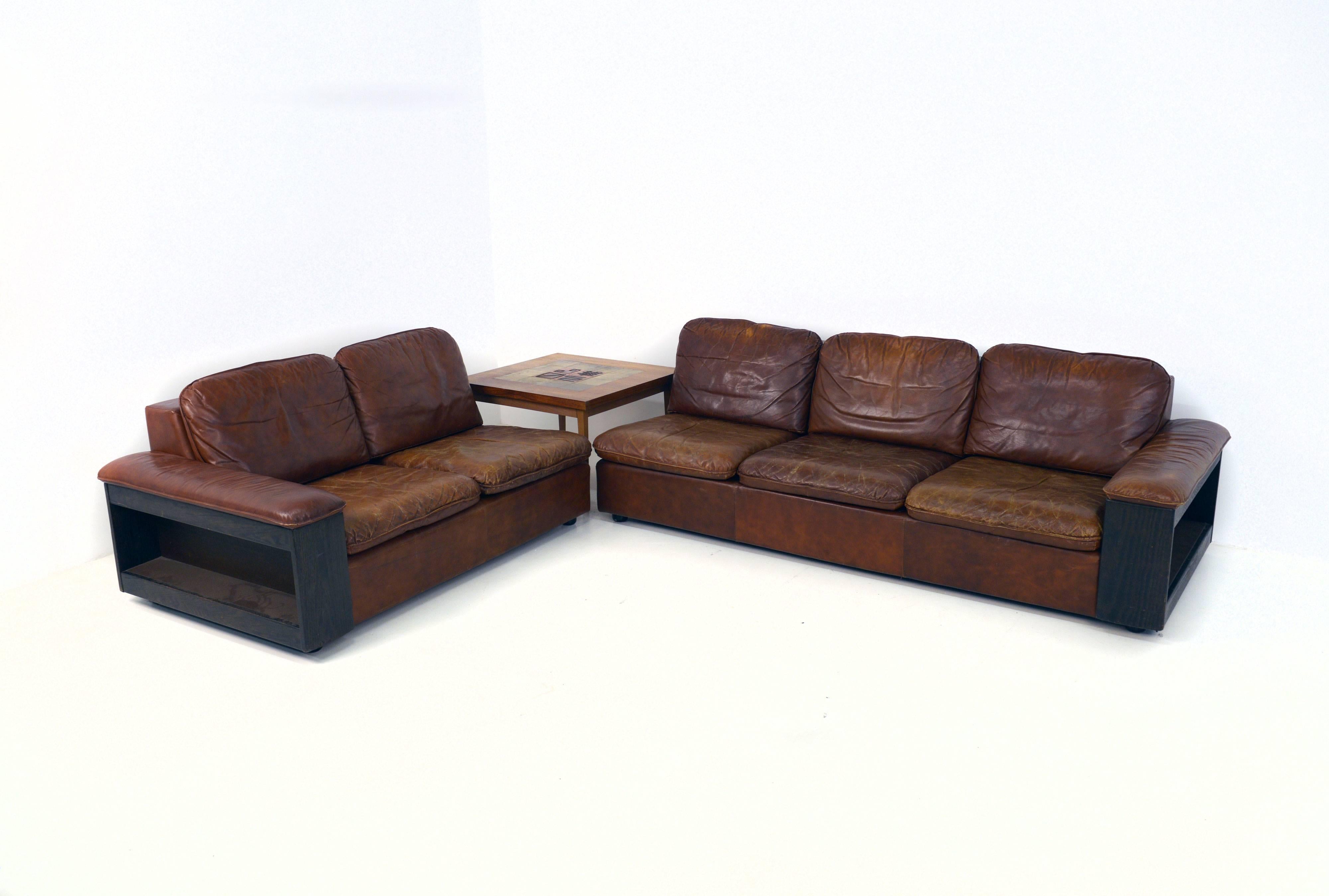 Very decorative five-seat leather sofa setting consisting of two parts.
On the back and side there is a bookcase.

Two-seat about: L 152, D 92, H 65 cm.
Three-seat about: L 215, D 92, H 65 cm.

Very nice vintage condition.
 