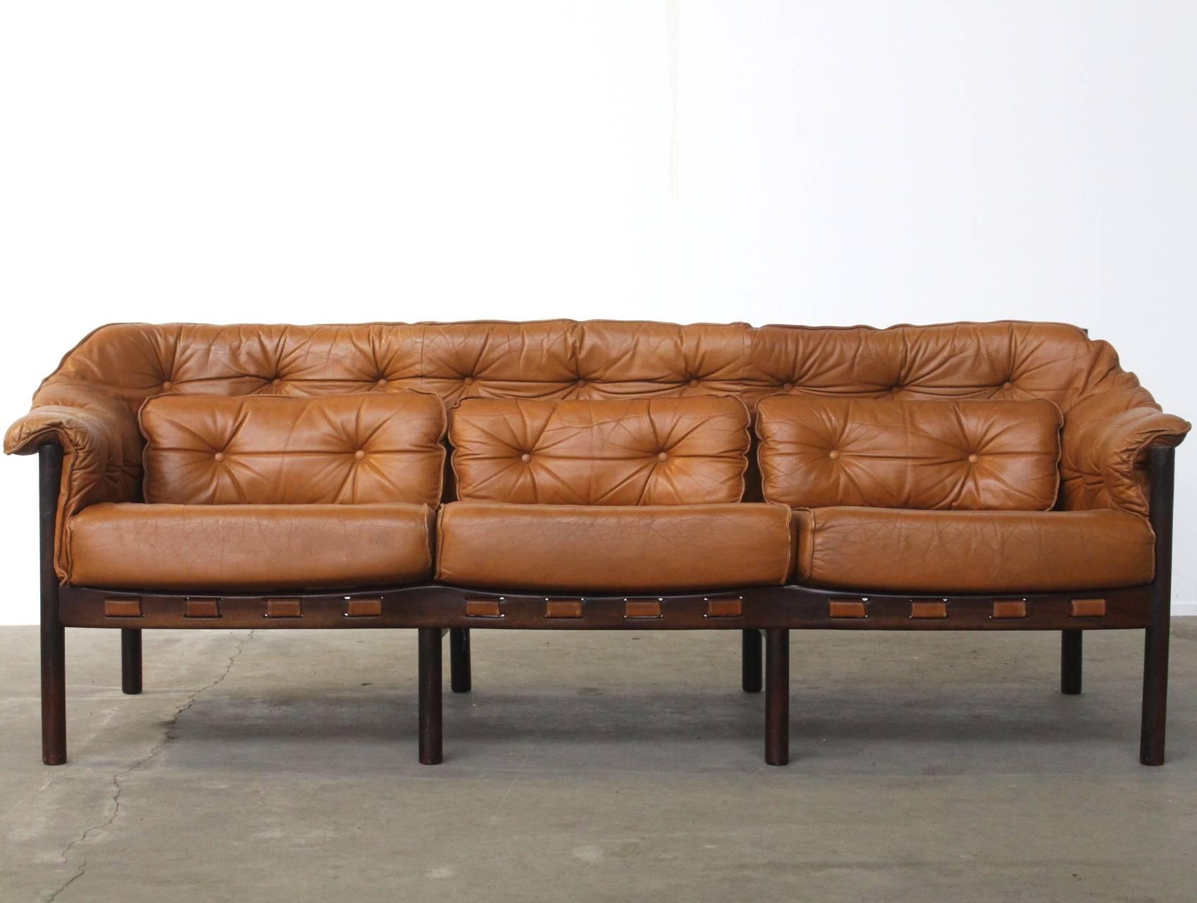 Beautiful tufted leather three-seat sofa by Arne Norell for Coja. All the original cushions are there and the condition of the leather is very good. The sofa frame is made of dark rosewood and the color is camel, which is quite rare. This item goes