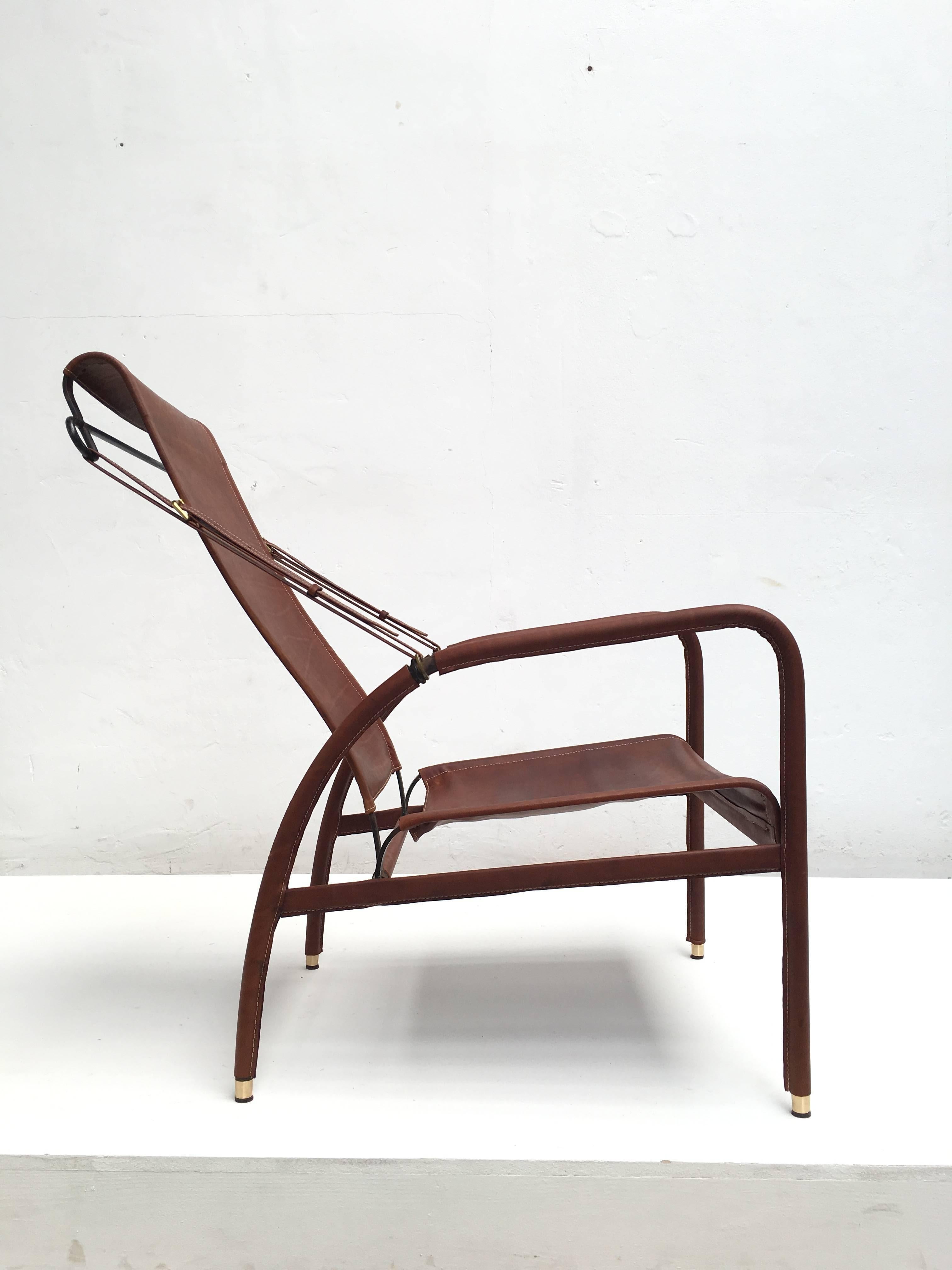 Handsome and rare Jacques Adnet lounge chair recently refinished in beautiful hand-stitched leather by specialist upholsterer 'Couch and Cover' in Antwerp. Lovely brass details to the feet, armrest finishers and buckles.

This chair was in a