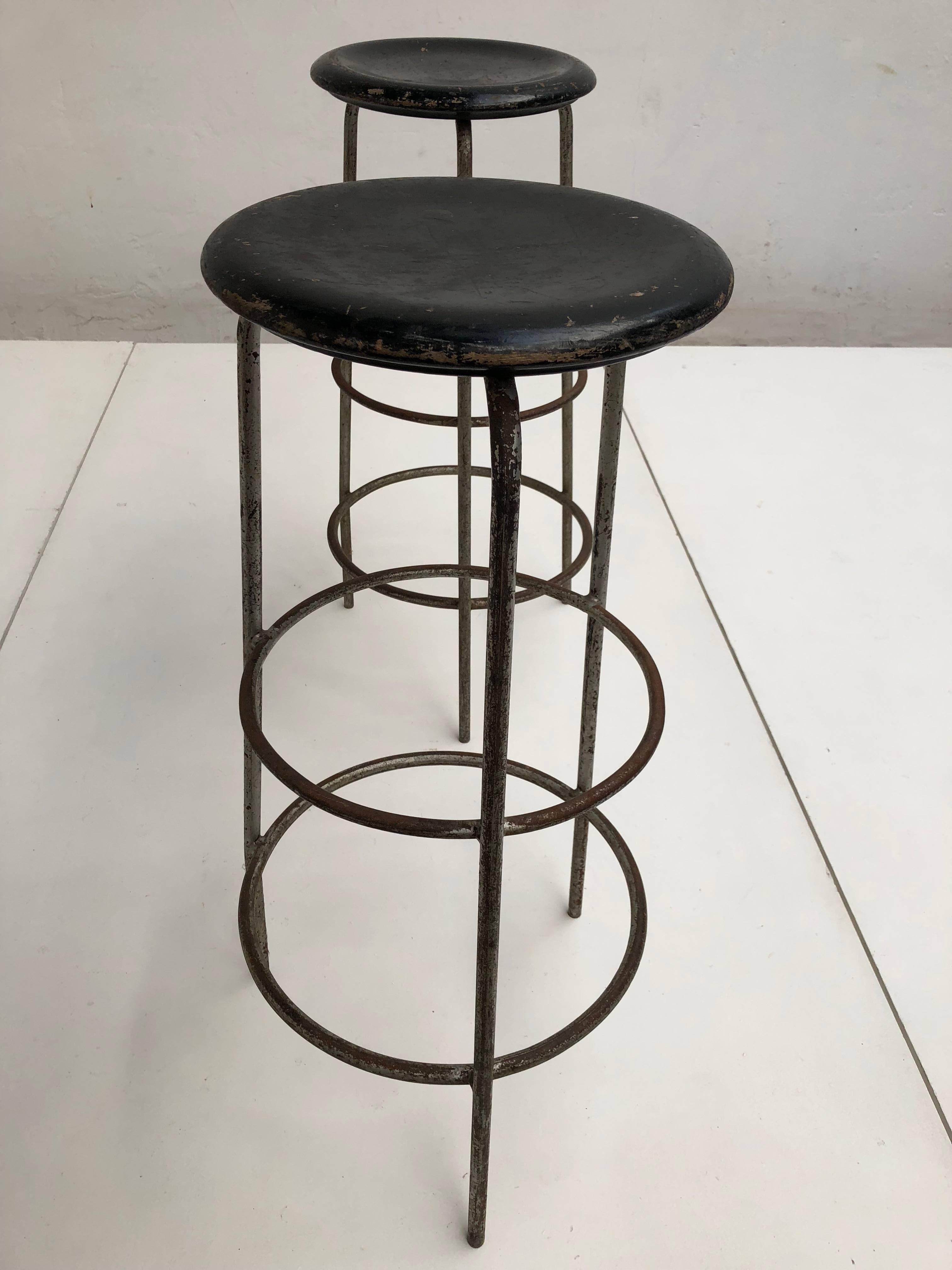 Pair of high working / bar stools that originated from a Swiss confection atelier 

Carved black lacquered wooden round seating on tubular steel grey enamelled legs

This pair of stools have a lovely old and aged patina from user wear consistent