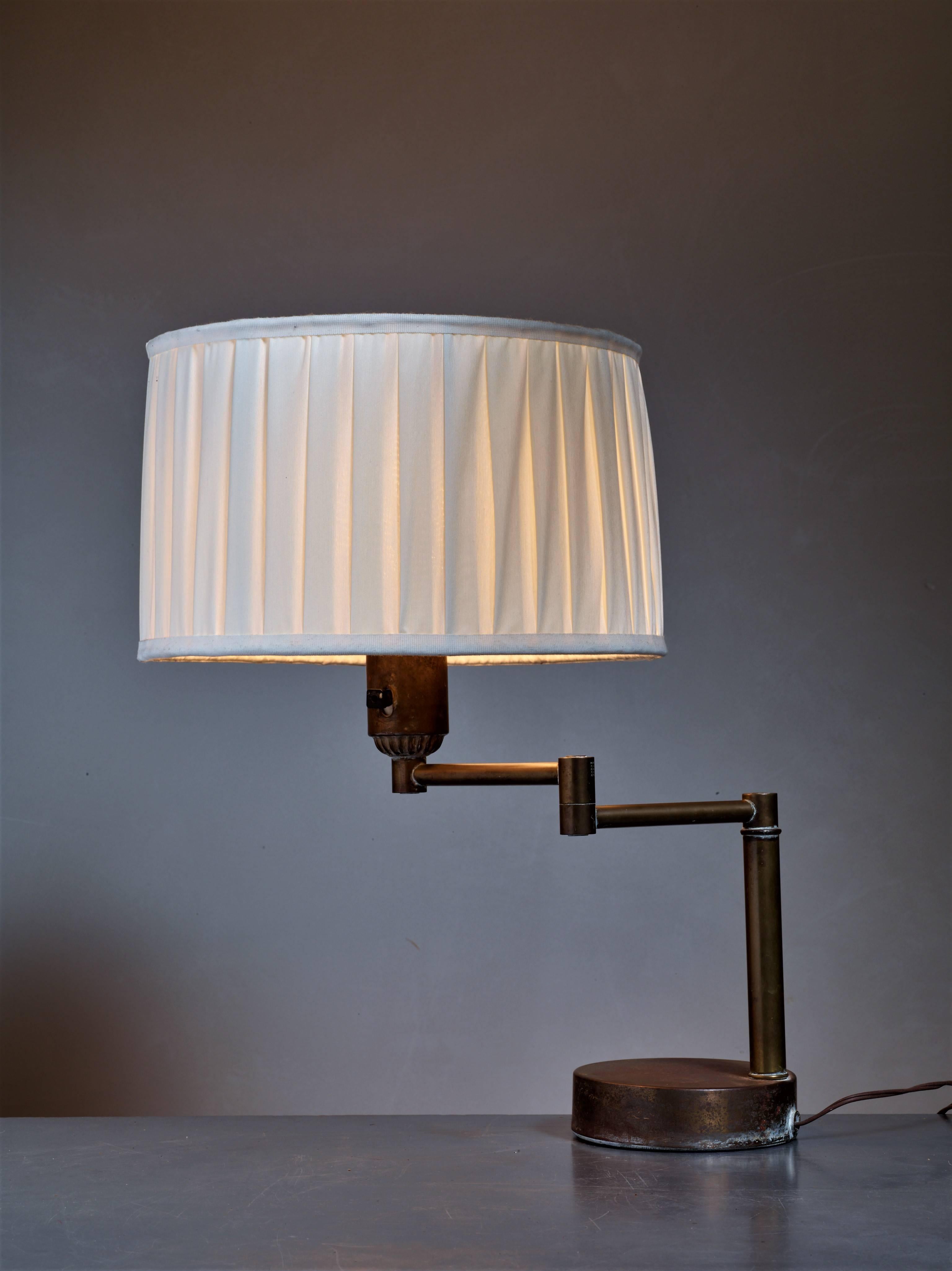 A Walter Von Nessen swing-arm table lamp with a milk glass diffuser and the original fabric shade. The lamp is a variation on his Classic stainless steel design from 1927. This base is made of brass with a beautiful patina.
The swing arm allows you
