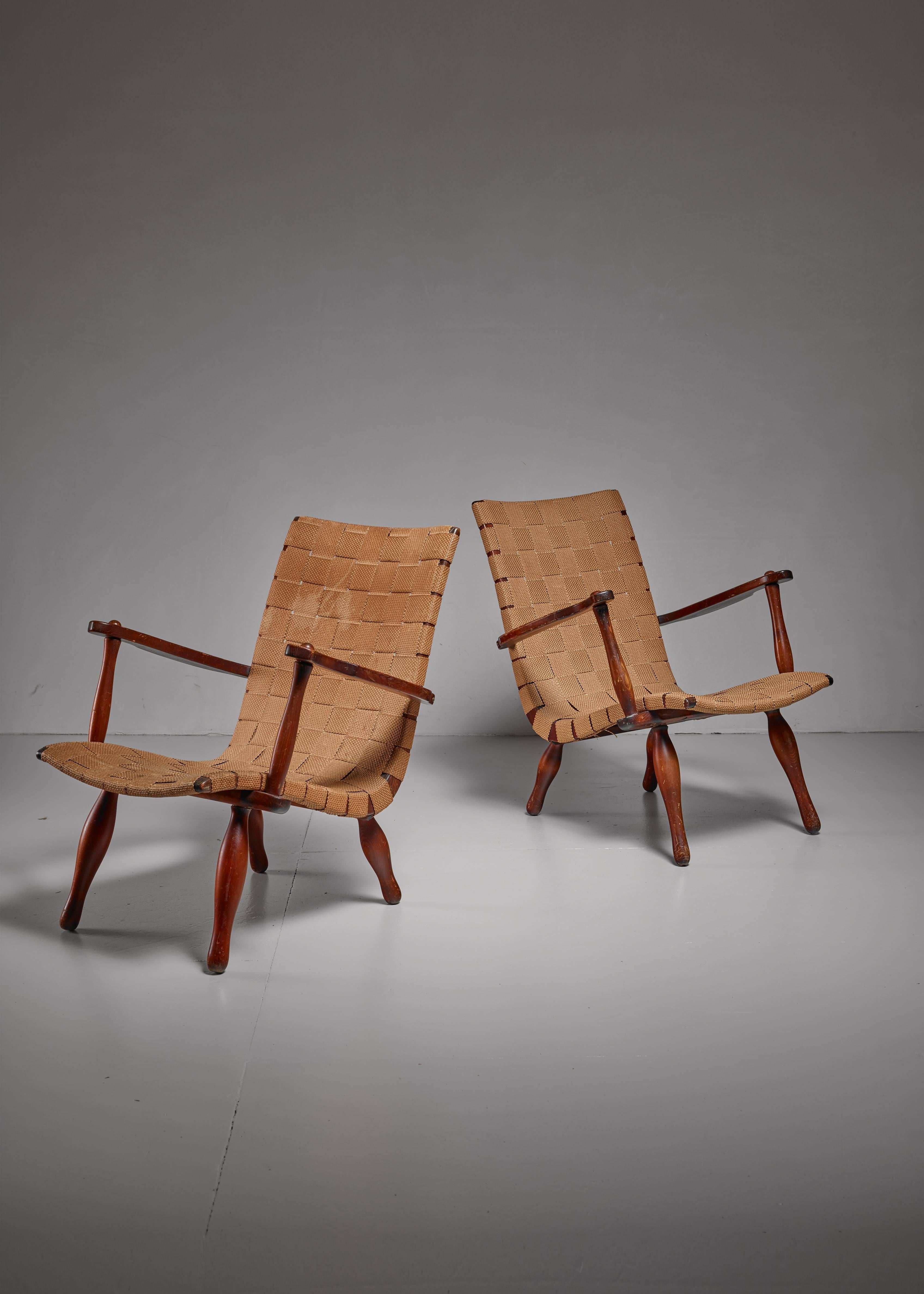 A pair of wooden lounge chairs in the style of Elias Svedberg for Nordiska, with a beige webbed canvas seating. The chairs have sculptural rounded legs and wide and curving armrests.