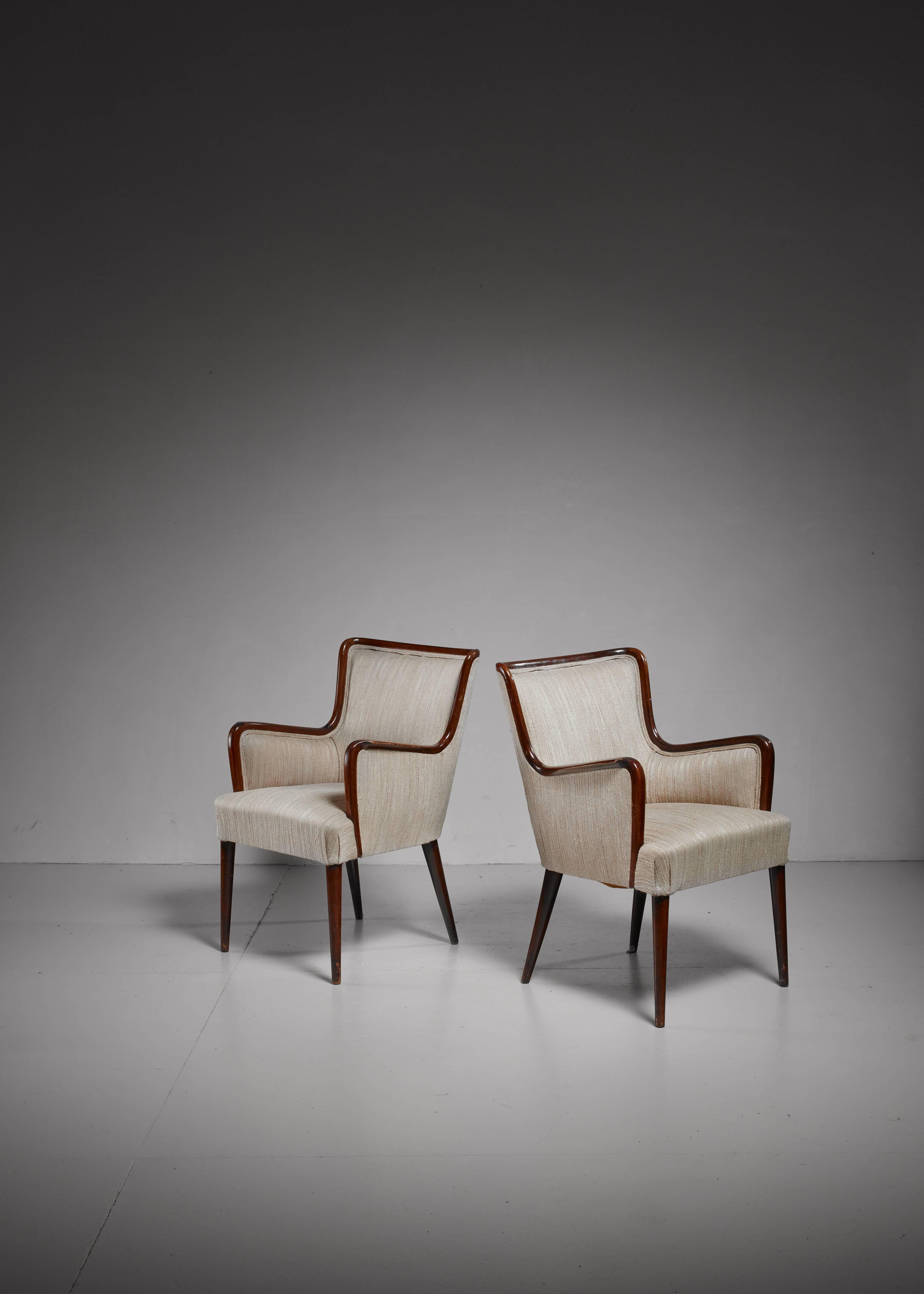 A pair of rare and original Osvaldo Borsani armchairs from the 1940s. The chairs are made of a rich and warm mahogany and a beige woven fabric upholstery. The subtle interplay of lines of the wooden frame and the slightly tapering feet makes these