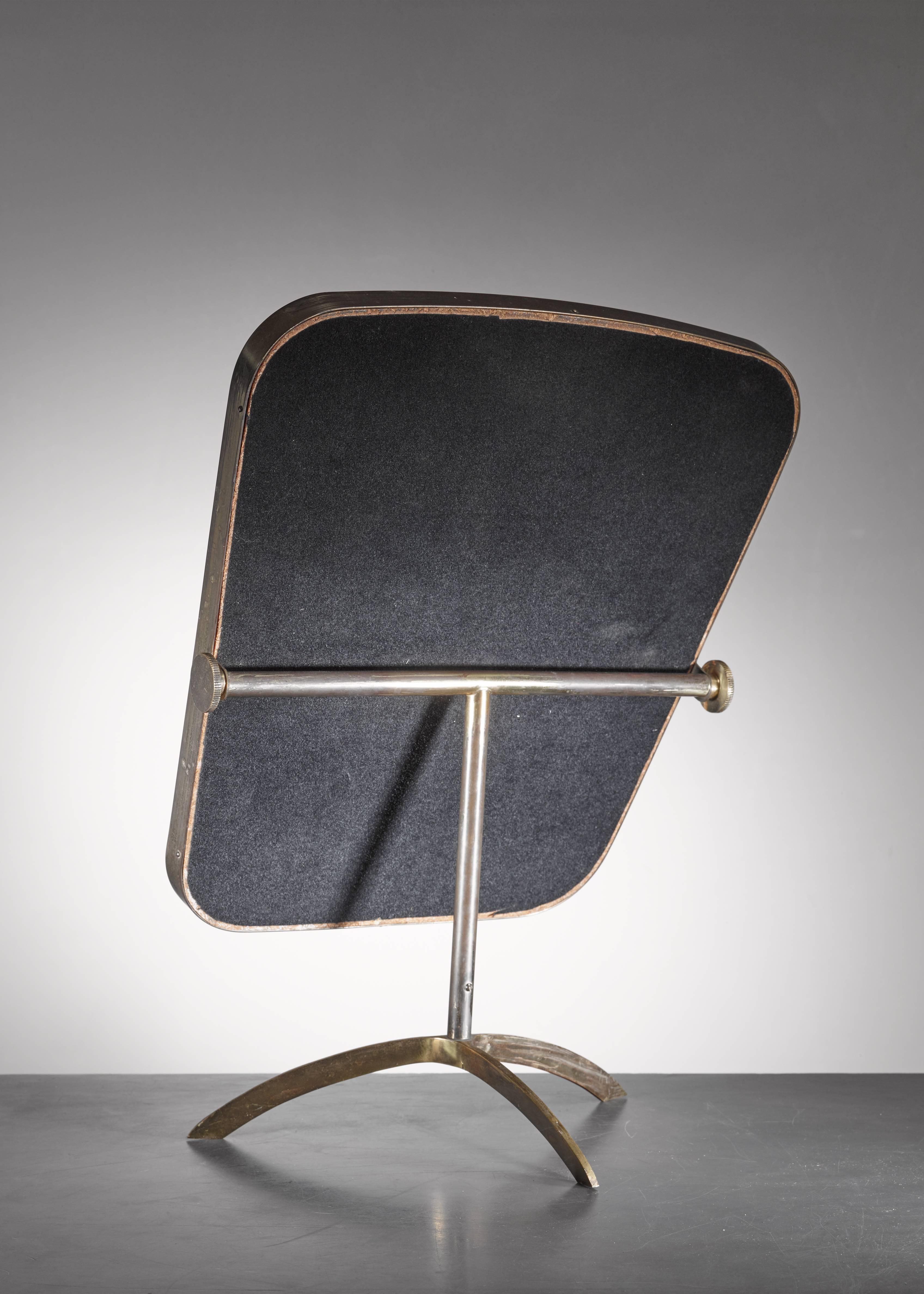 An adjustable brass console mirror on a tripod foot with a small white inside rim. The back of the mirror is covered with a black fabric.

