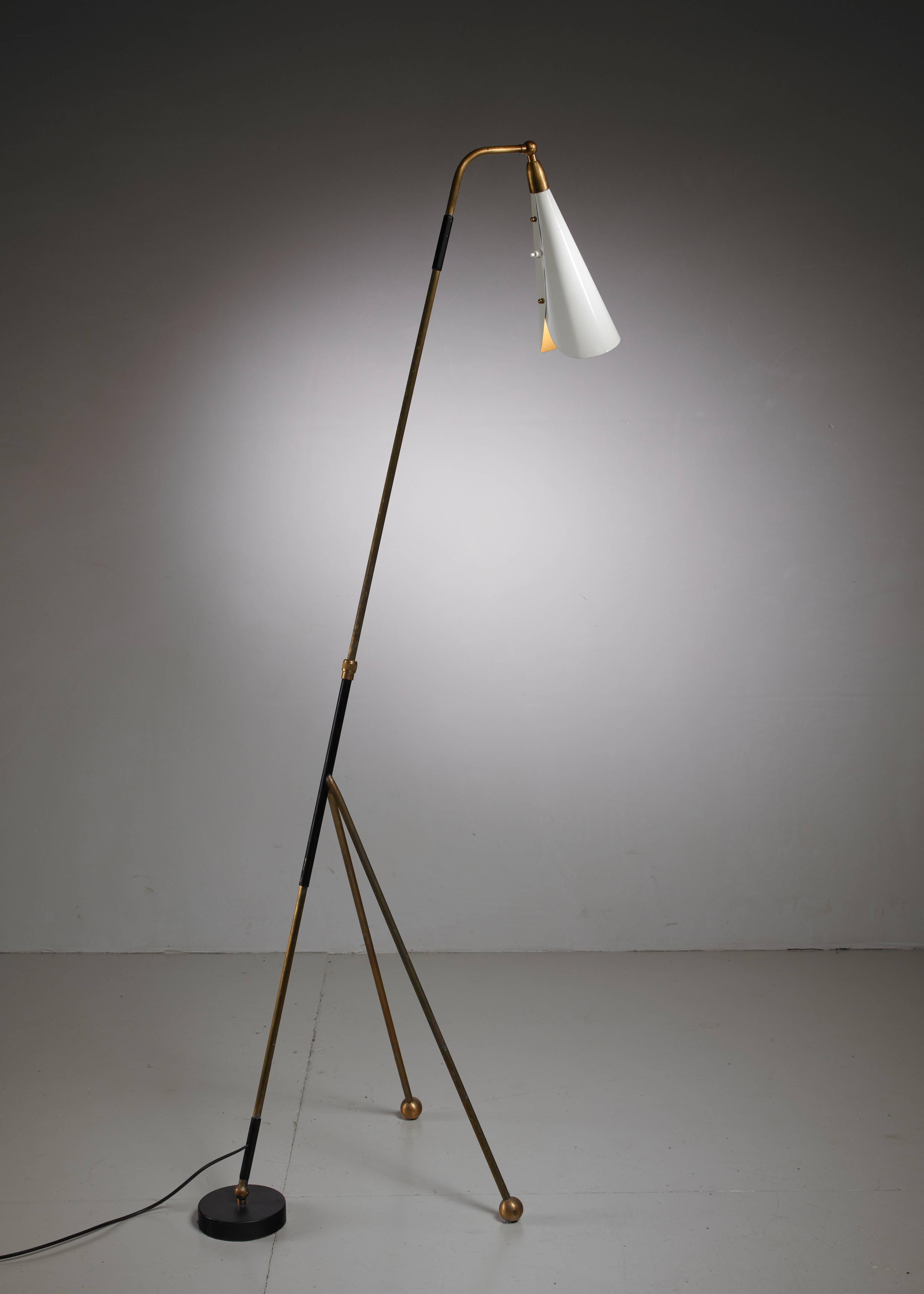 An Italian tripod floor lamp in the style of Arteluce and Arredoluce. It is made of brass with a white metal shade of which the angle can be adjusted from a 45 to 180 degrees. The counterweight at the floor keeps the lamp in position. Perfect