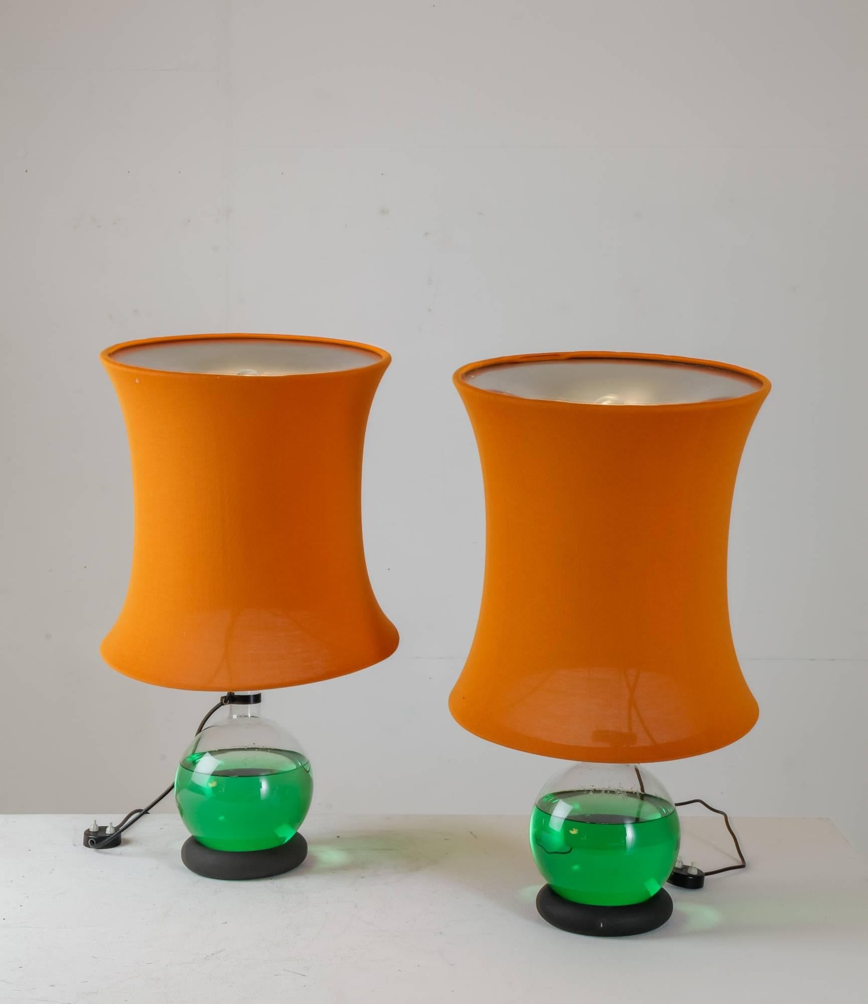 A set of two Lotus table lamps designed by Gianfranco Frattini for Meroni in 1966. The lamps are made of a lacquered wooden ring base on which a glass flask filled with transparent green liquid stands, creating a lens-like optical effect. The colour