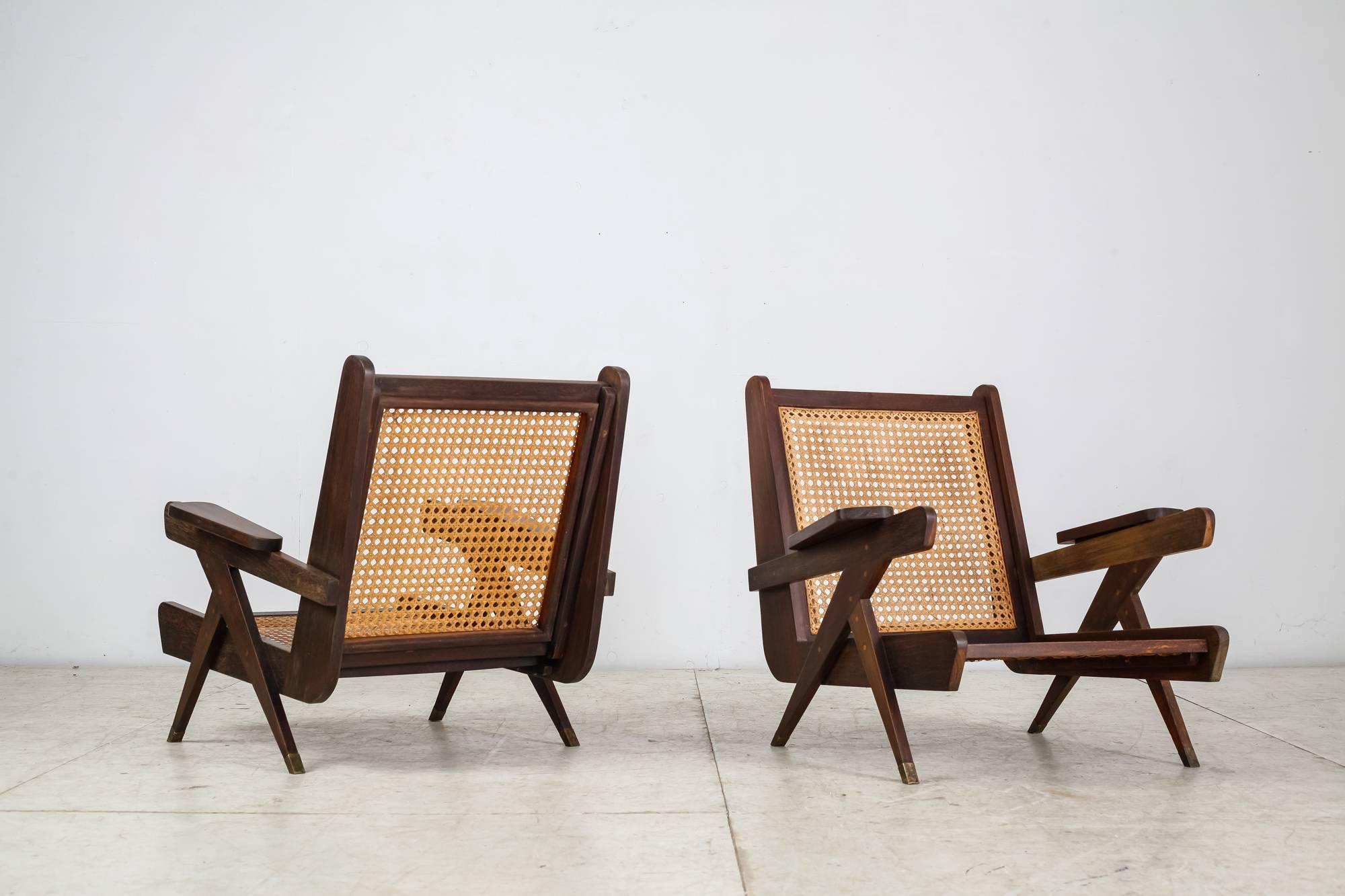 A pair of modernist French armchairs, strongly reminiscent of the work of Pierre Jeanneret. The chairs are made of a dark teak frame with tapering arm pads, a woven cane seating and bronze feet. Both the wood and bronze have a lovely patina and are