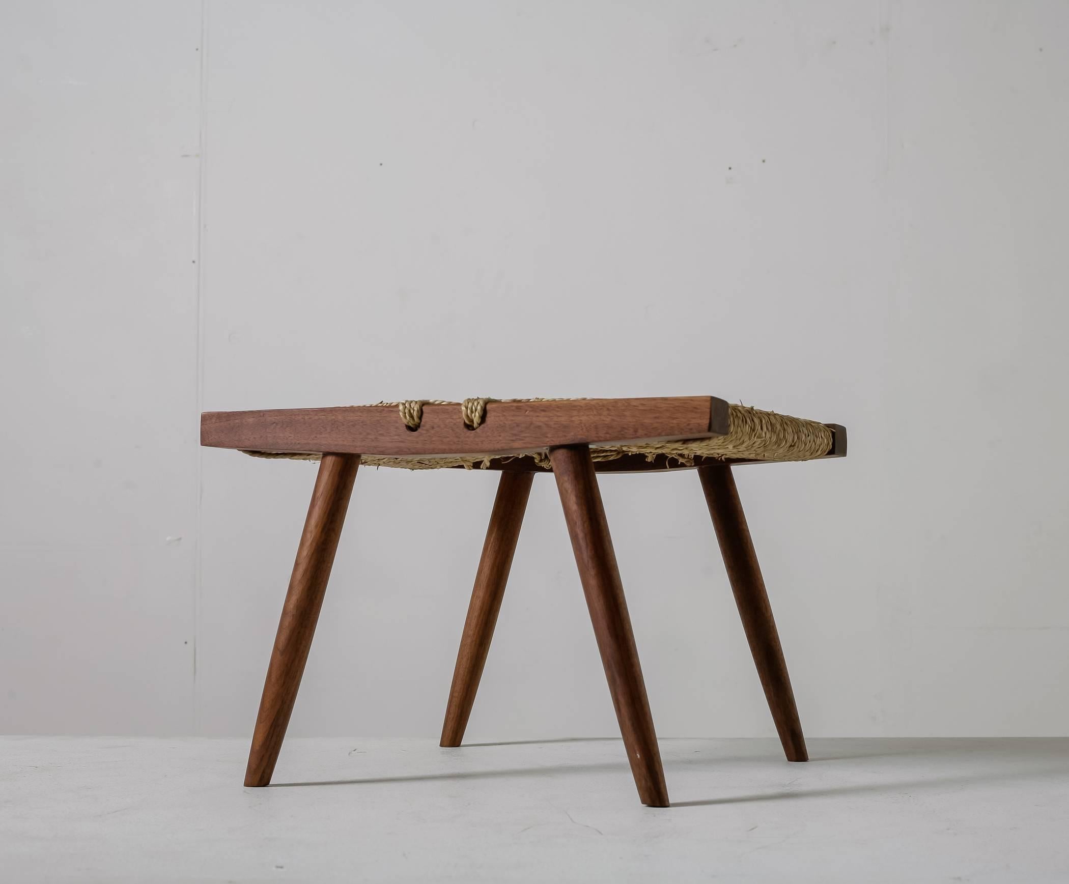 A George Nakashima stool made of a walnut frame with a grass rope seating. This rectangular stool stands on four tapering legs and is in a very good condition.