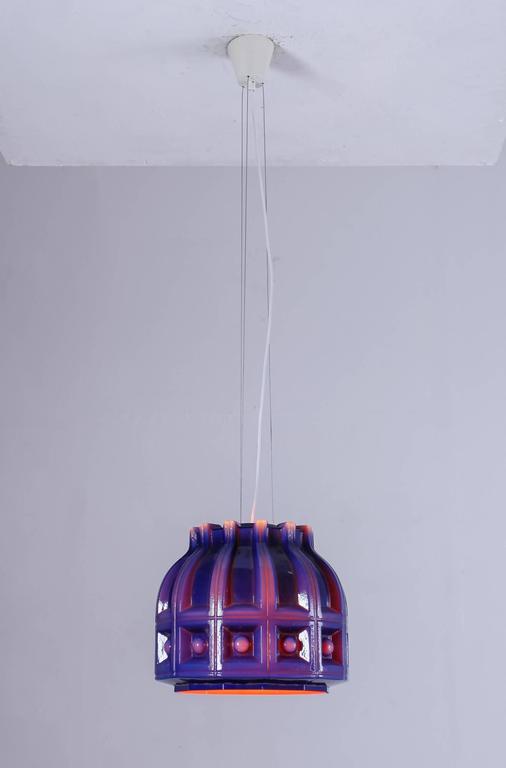A Helena Tynell pendant made of double layered glass for Flygsfors, Sweden. The outer layer is made of a thick, textured blue glass and the layer on the inside is orange. The orange gives the light a beautiful and warm color.
The lamp hangs from