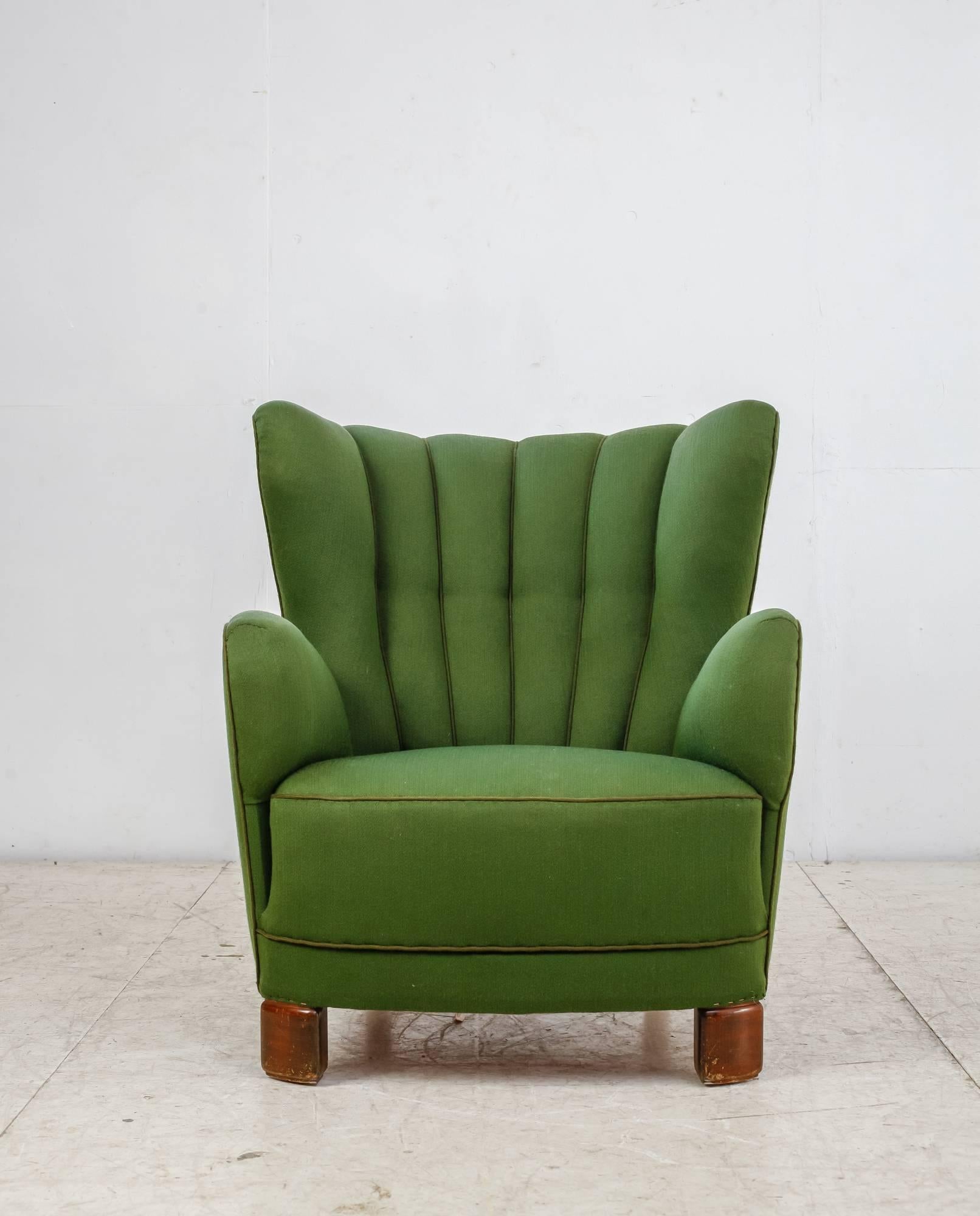 A 1940s Danish wingback lounge chair with a green wool upholstery with brown trim. The chair stands on stained beech legs, the ones in the front with a rounded shape.

A very comfortable and luxurious chair with upholstery in a great condition.

