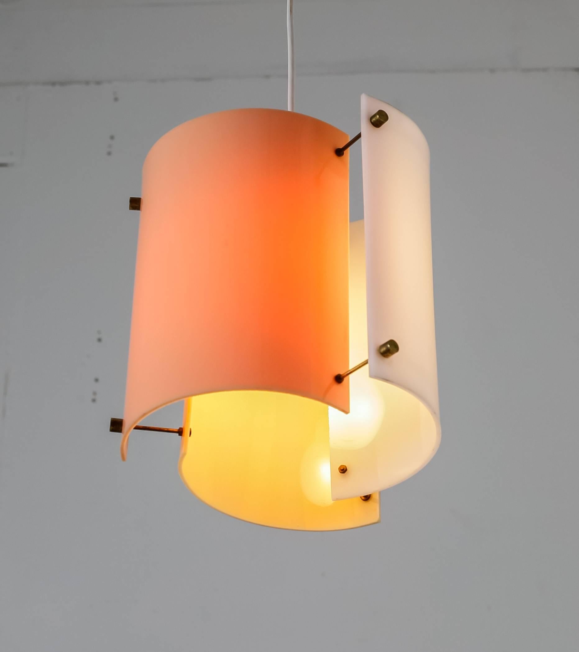 A Yki Nummi 1960s pendant lamp for Orno, Finland. The lamp is made of three semicircular plexiglass elements in different colors (peach, yellow and orange), held together with thin brass rods. The colored plexiglass creates a beautiful, atmospheric