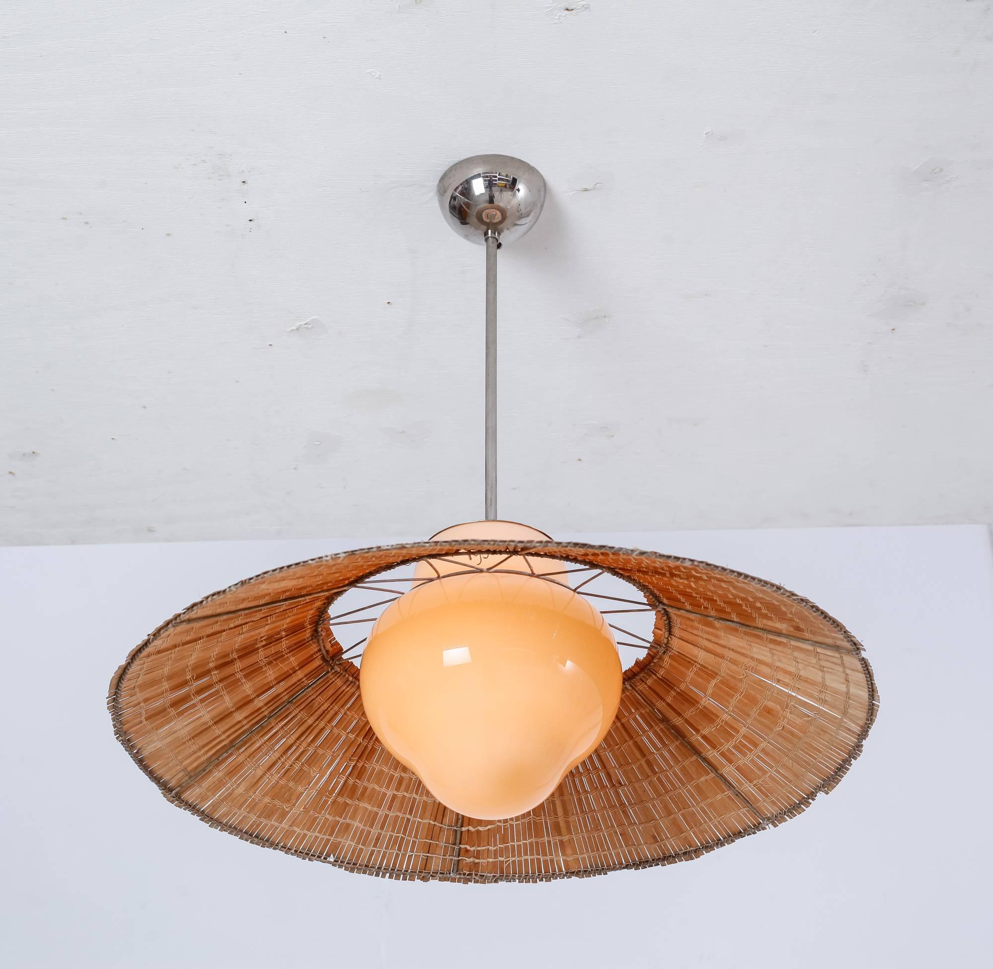 A model 1088 pendant by Gunilla Jung for Orno. The lamp is made of a beige opaline glass diffuser with the round shade resting on it. The shade is made of thin rattan strips, woven together.

 