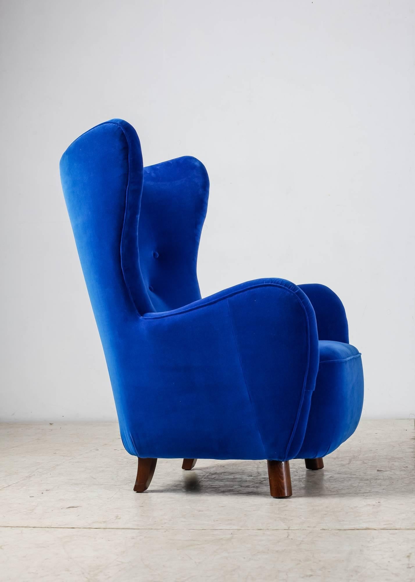 A 1940s wingback lounge chair attributed to Mogens Lassen. It stands on stained beech legs, round in front and rectangular in the back.
The chair has been professionally reupholstered in our atelier with a beautiful royal blue velour.