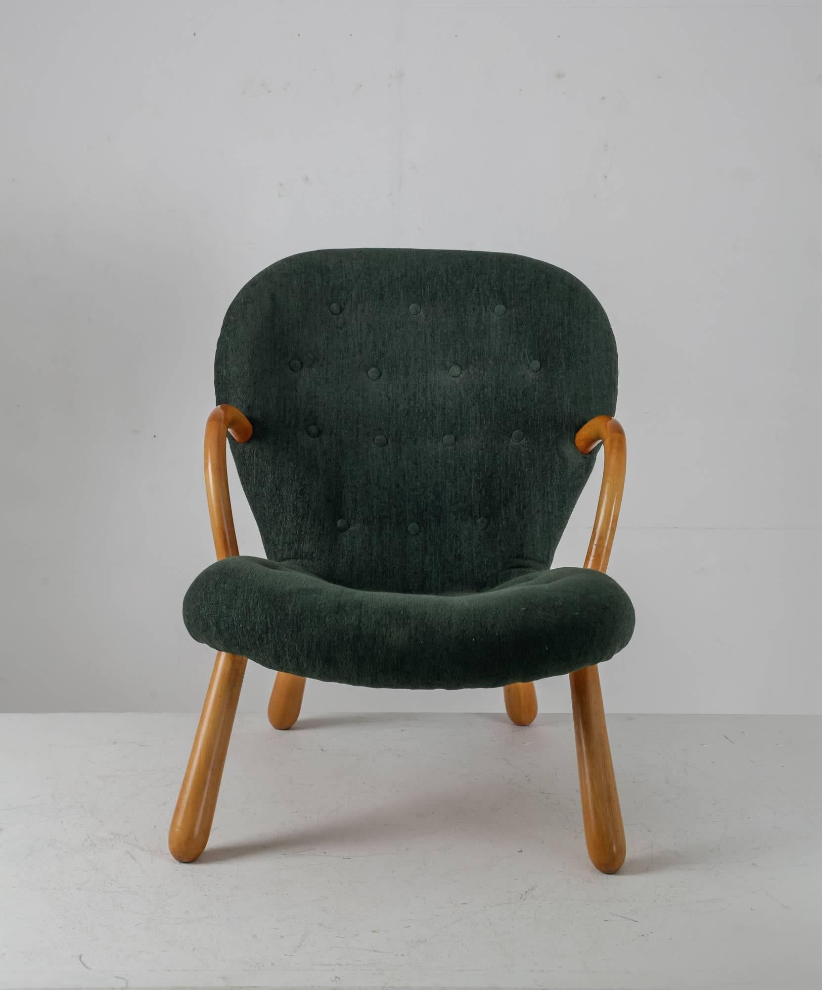 A Musling (clam) chair by Philip Arctander. The chair is made of a lacquered beech frame and a dark green upholstery. The wooden armrests are molded and the legs are rounded, giving the chair an organic shape and the inspiration for its