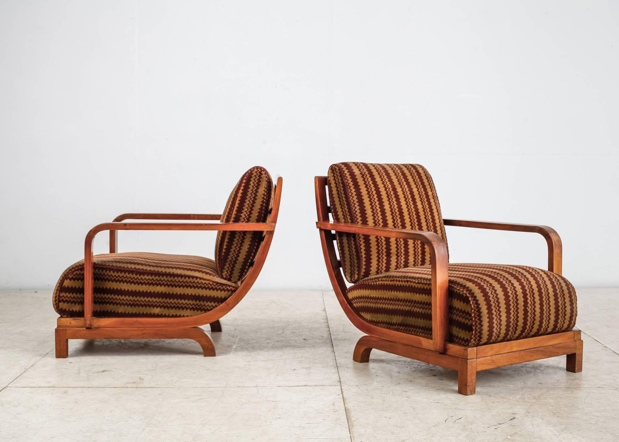 A pair of large Art Deco lounge chairs, made of a curved mahogany frame with loose, shaped cushions. The cushions have a beautiful velour upholstery with a geometric pattern, fitting the design of the chairs and the period they were made in. The