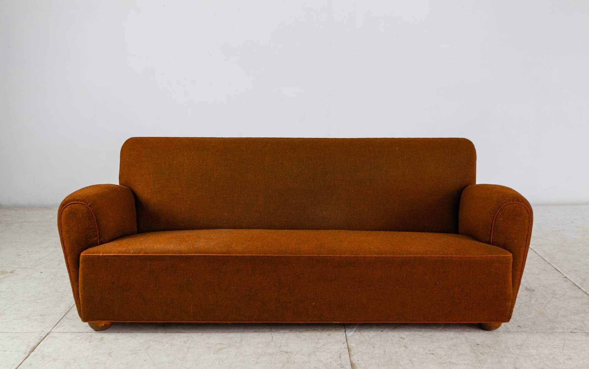 A three-seat sofa with a brown wool upholstery, standing on stained beech feet. The sofa has a wonderful round shape and is structurally still in an excellent condition, but the upholstery has wear. It can be professionally reupholstered in our