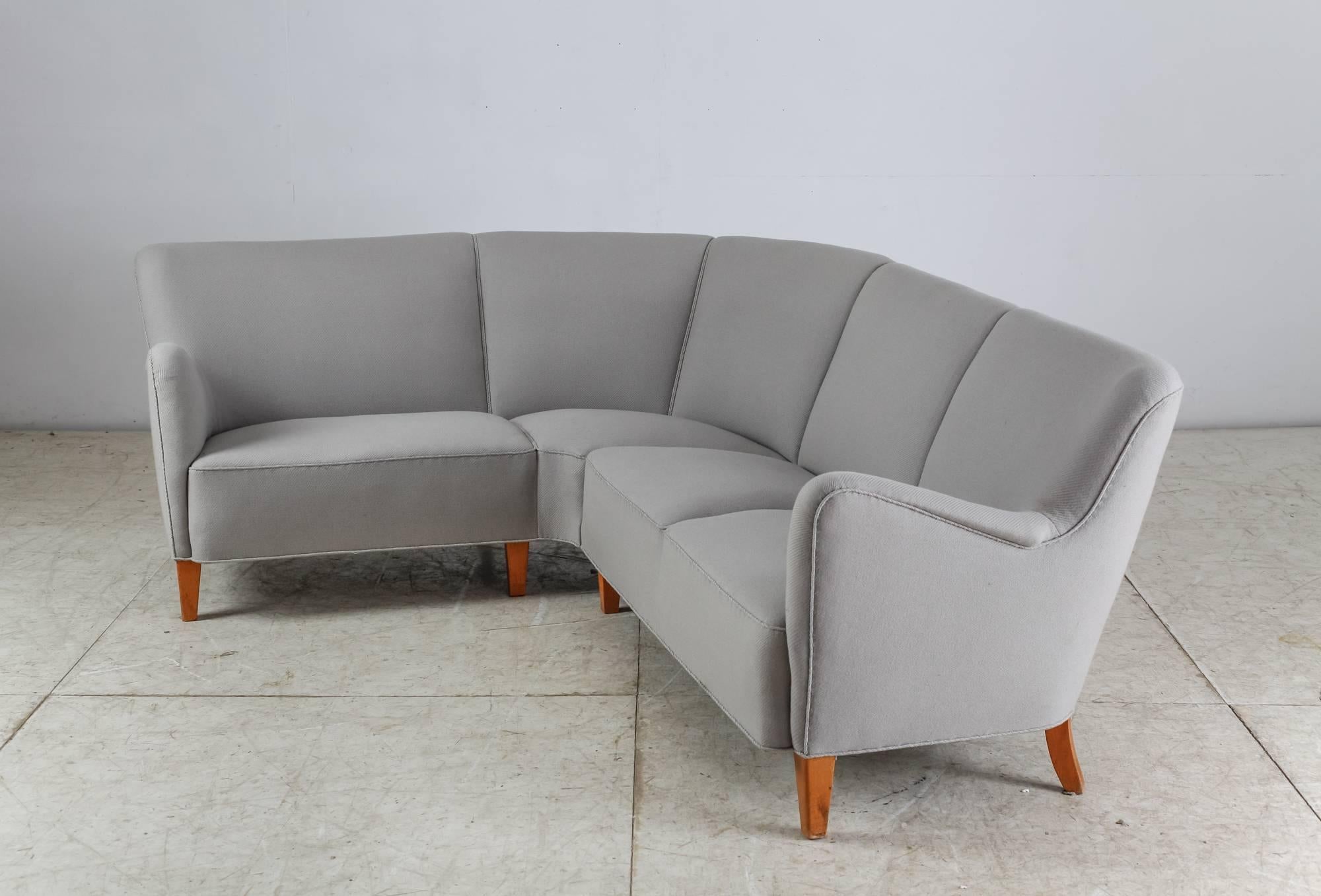 A large Danish corner sofa standing on eight stained beech legs and upholstered with a light grey wool. The sofa can be easily disassembled into two parts.
The wool has age-related wear and it can be professionally reupholstered in our in-house