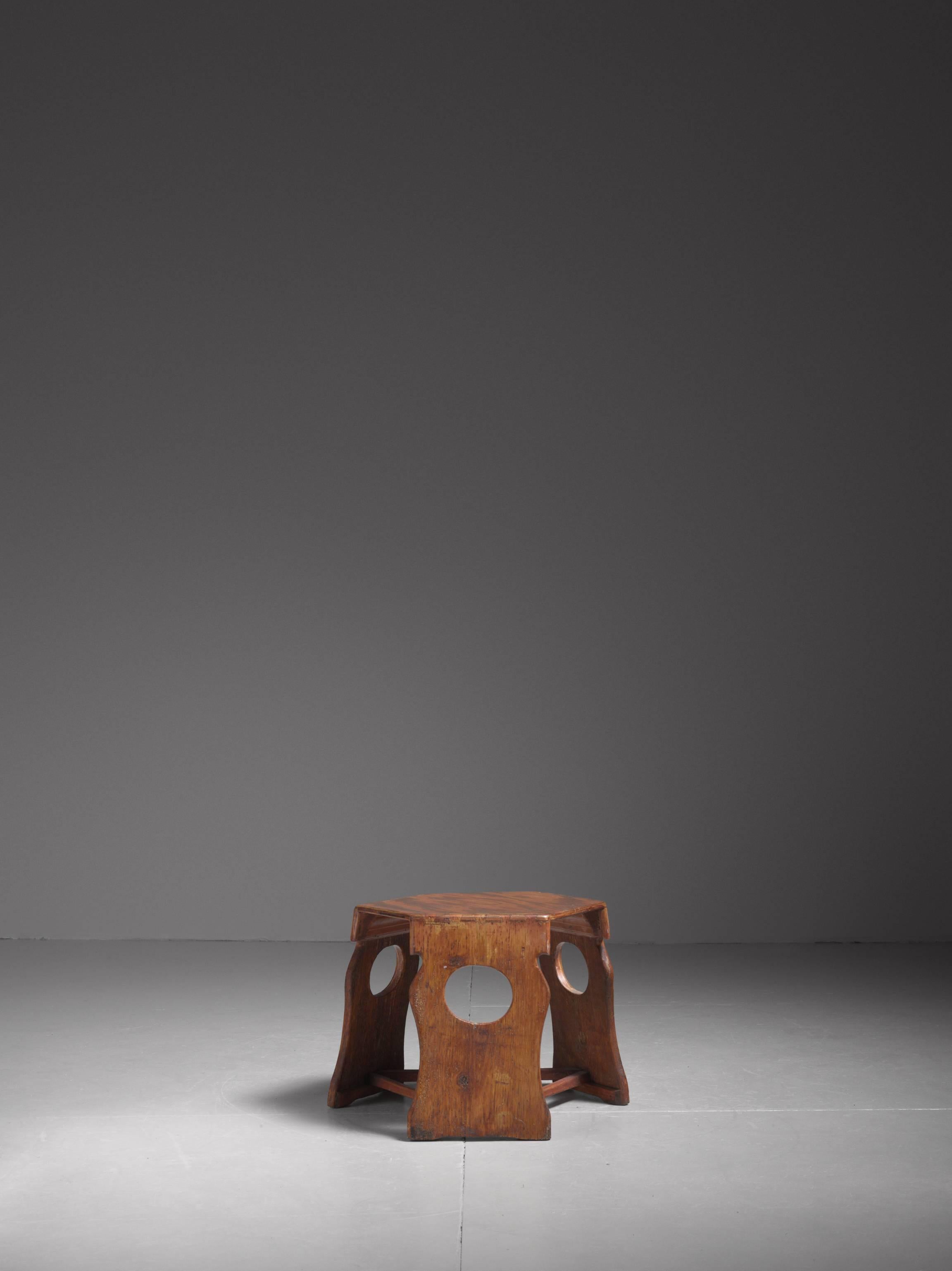 A hexagonal stool or side table made of pine, with three sculpted legs with beautiful wood connections.

A unique, craft fully made piece with a strong patina on the wood.