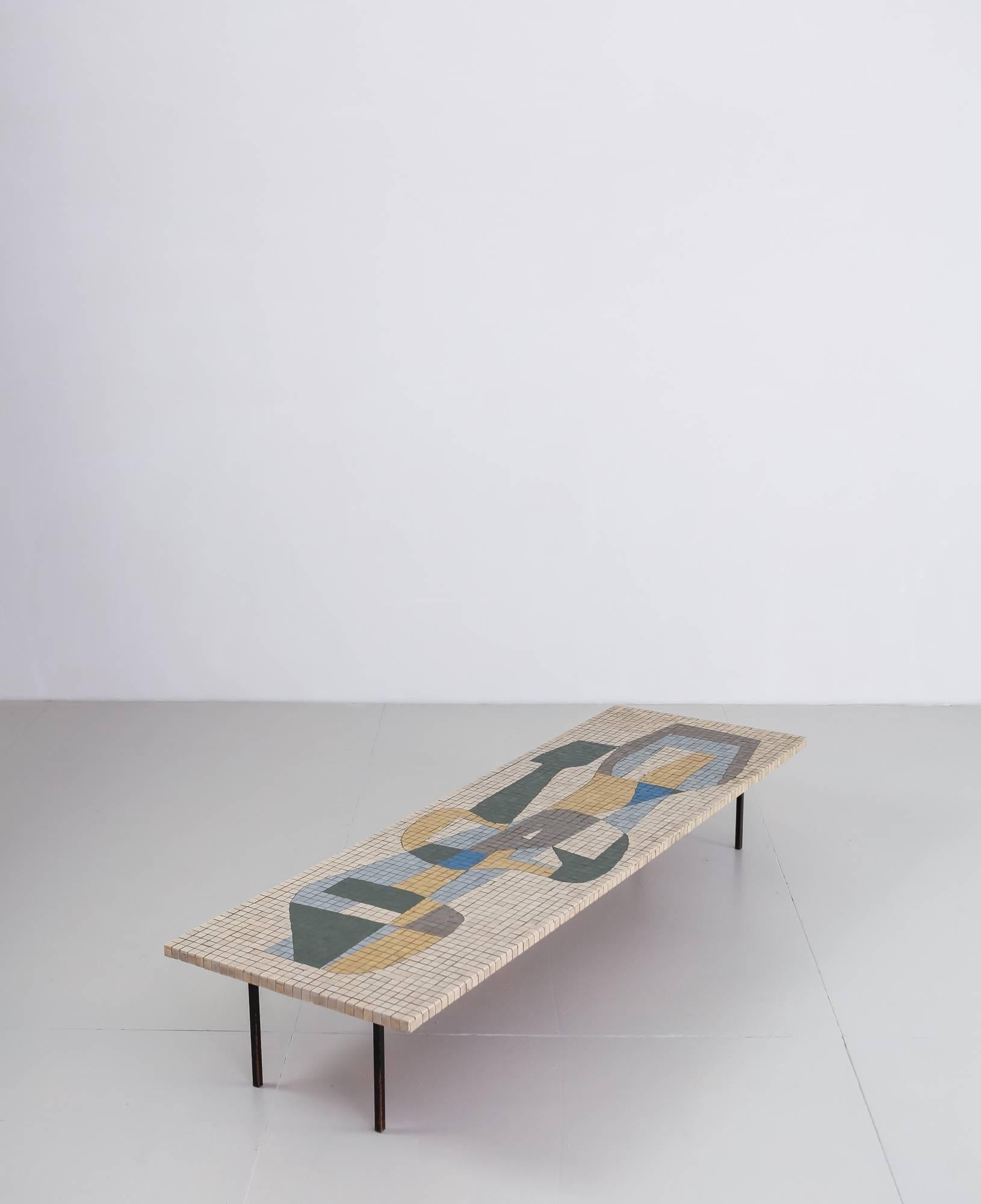 A long, rectangular coffee table with an abstract, Mid-Century Modernist mosaic tile composition, on a black lacquered metal frame. The edges of the top have tiles all around.