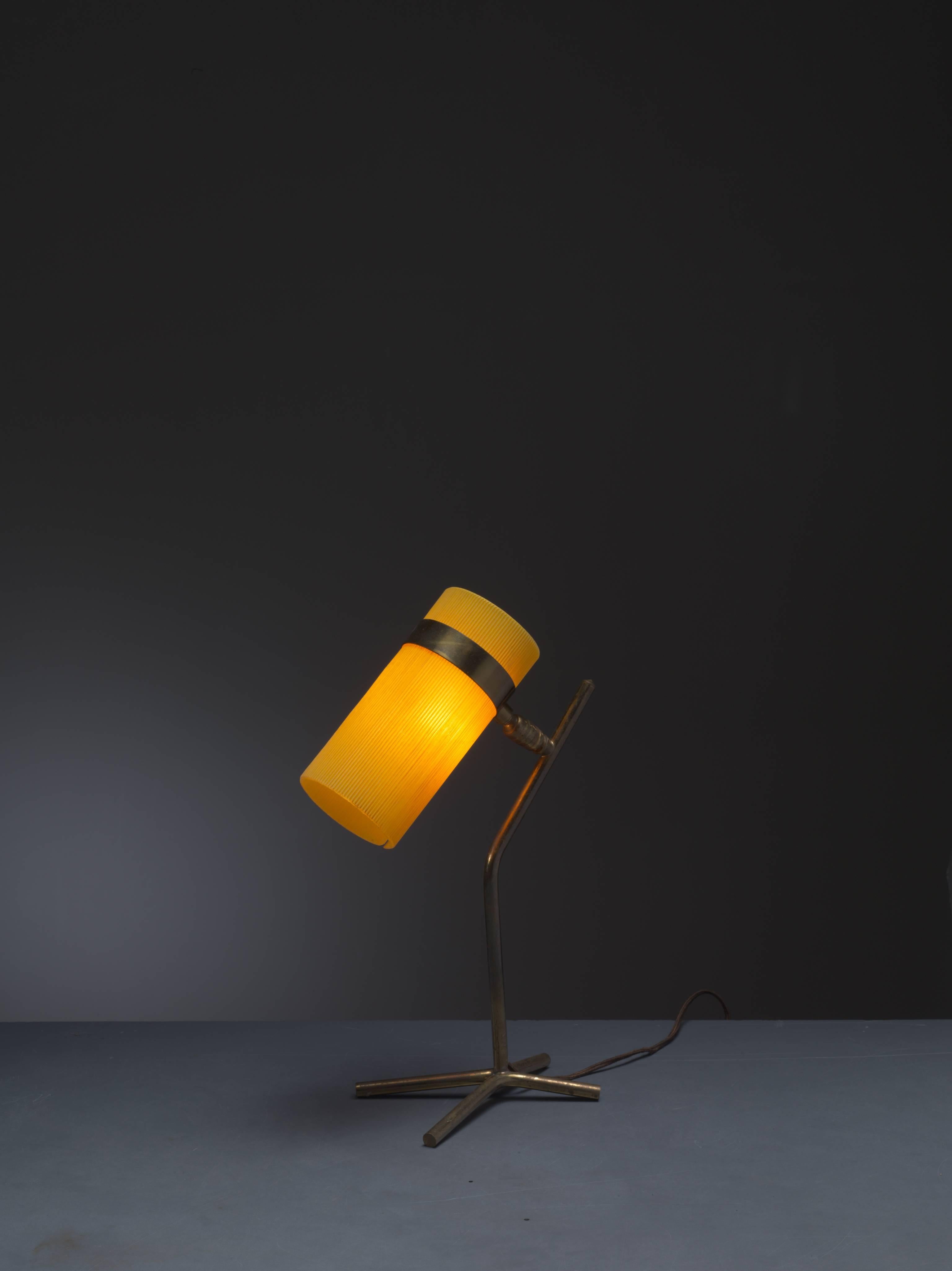 A petite French table lamp reminiscent of the work of Boris Lacroix and Pierre Guariche, made of a yellow plastic cylinder shade on brass feet. The ball construction allows the shade to be turned 360 degree.