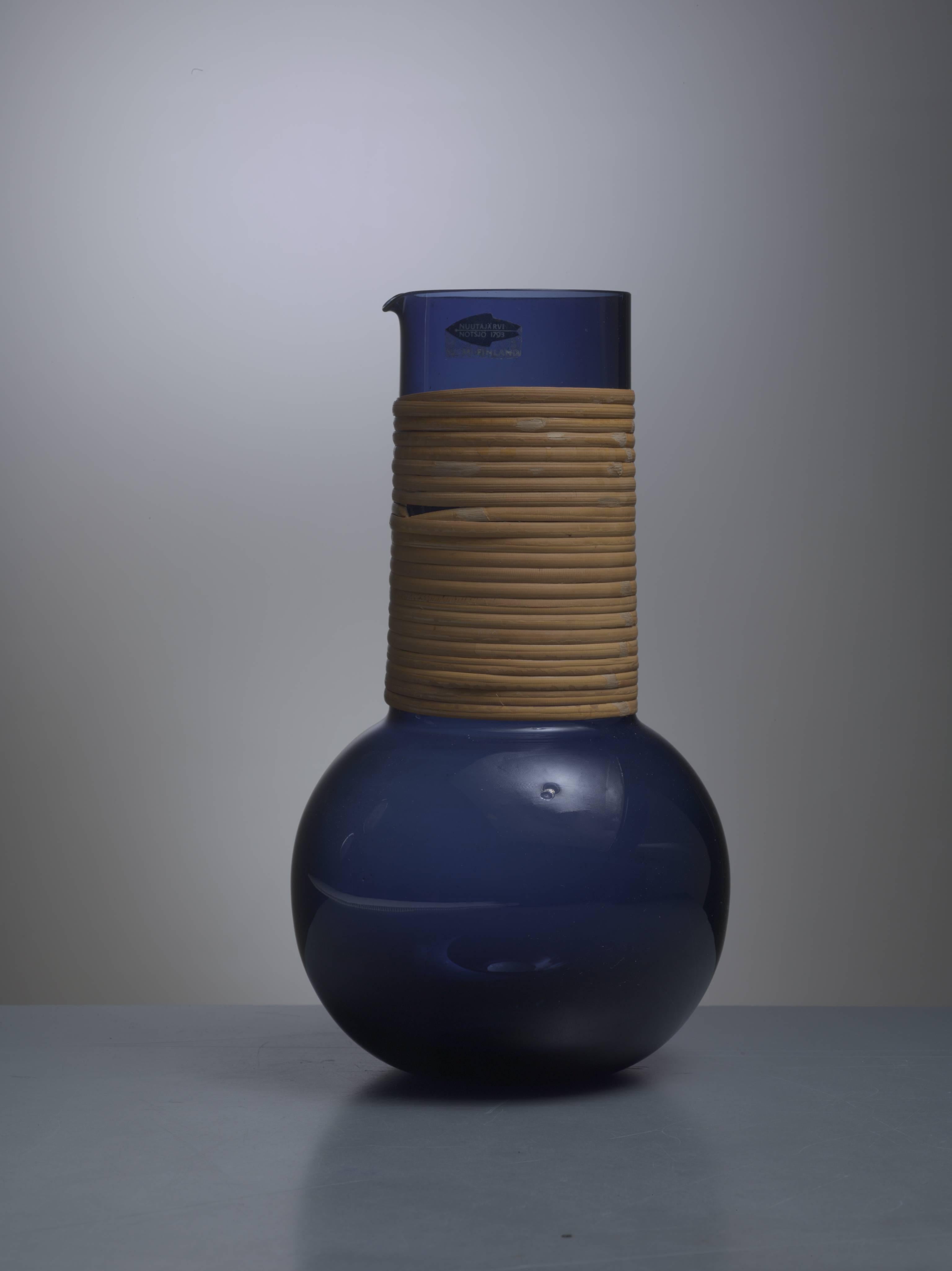 A blue glass pitcher with rattan wrapped around it. The pitcher was designed by Kaj Franck for Nuutajärvi, Finland, in 1955.
Labeled by Nuutajärvi and in a wonderful condition.