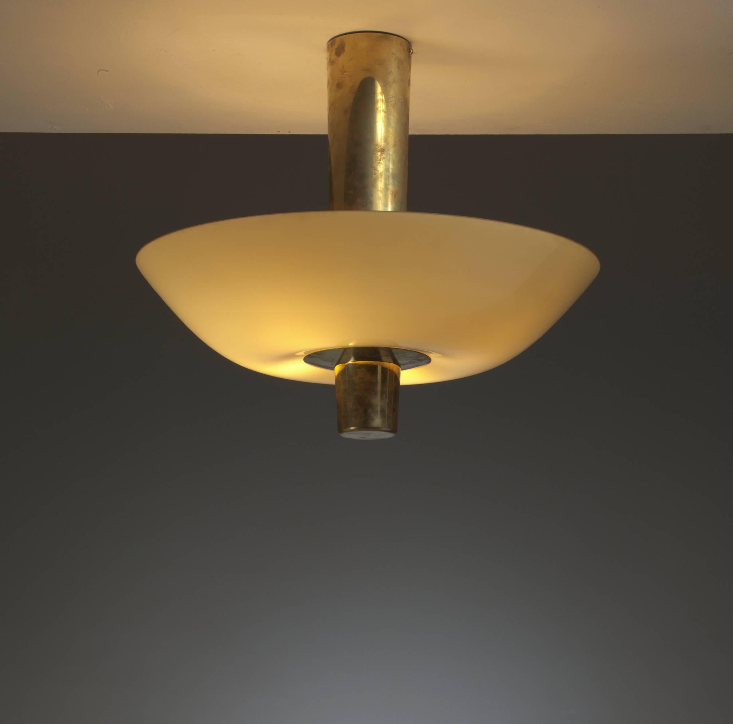 A Paavo Tynell model 9053 ceiling lamp for Idman with a long brass cylindrical stem holding four lamps inside the light yellow glass shade.
The chandelier is in a perfect condition and matches very well with the other 9053 Tynell flush mount in our