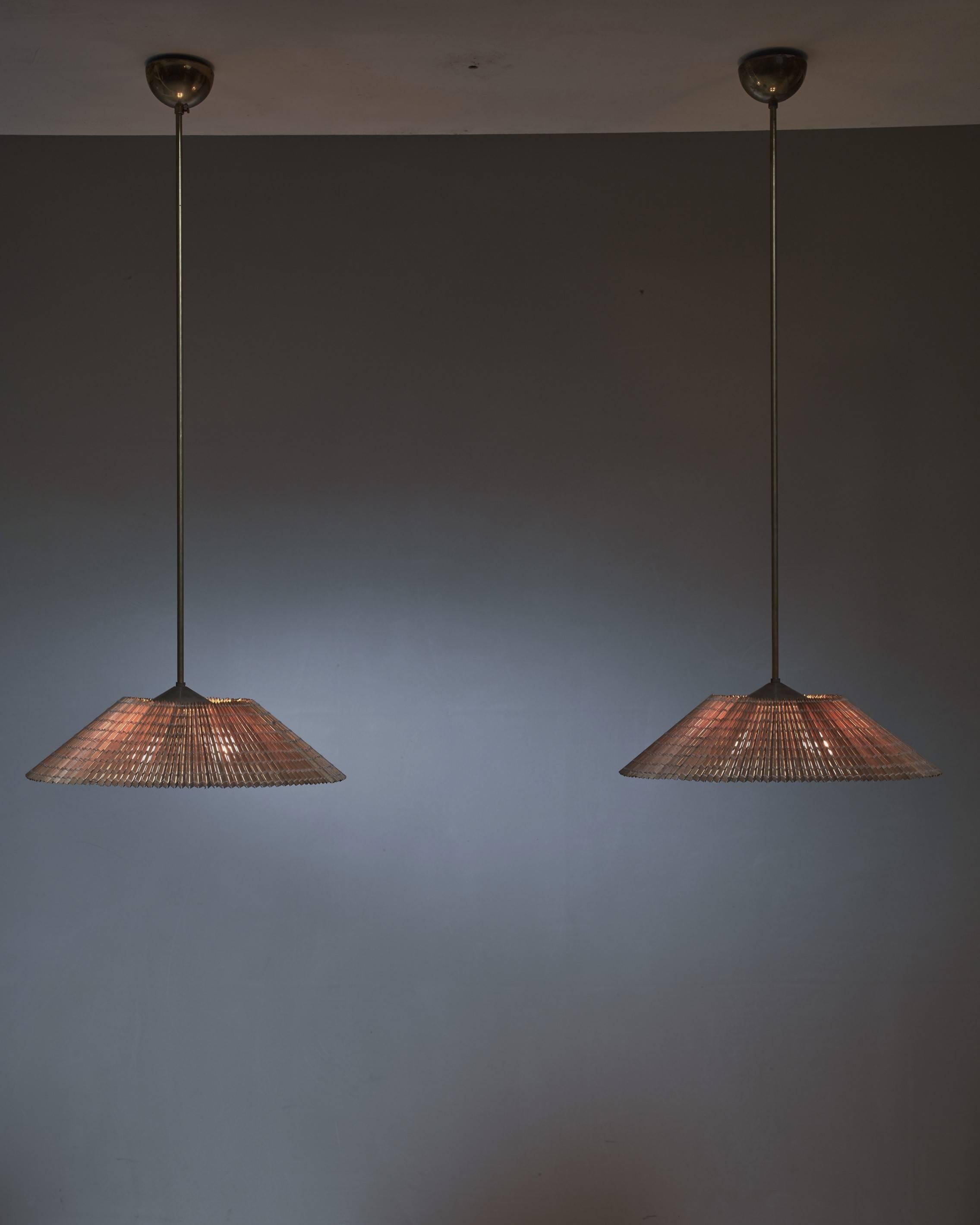 A pair of Paavo Tynell pendant lamps with four light bulbs for Idman. The shades of the lamps are made of thin strips of wood, held together by woven threads.
The lamps have a frosted glass diffuser underneath, a brass cap on top and are connected