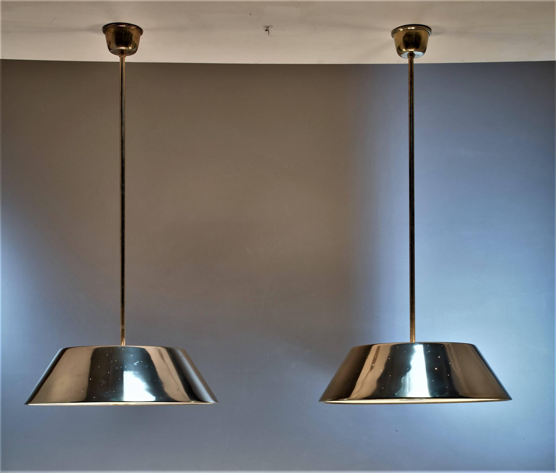 A pair of large Paavo Tynell brass pendant lamps with four-light bulbs. The shades have pin point perforations and a frosted glass diffuser. They have the combination of minimalism and richness that is typical for Paavo Tynell measures: 22.83 inch