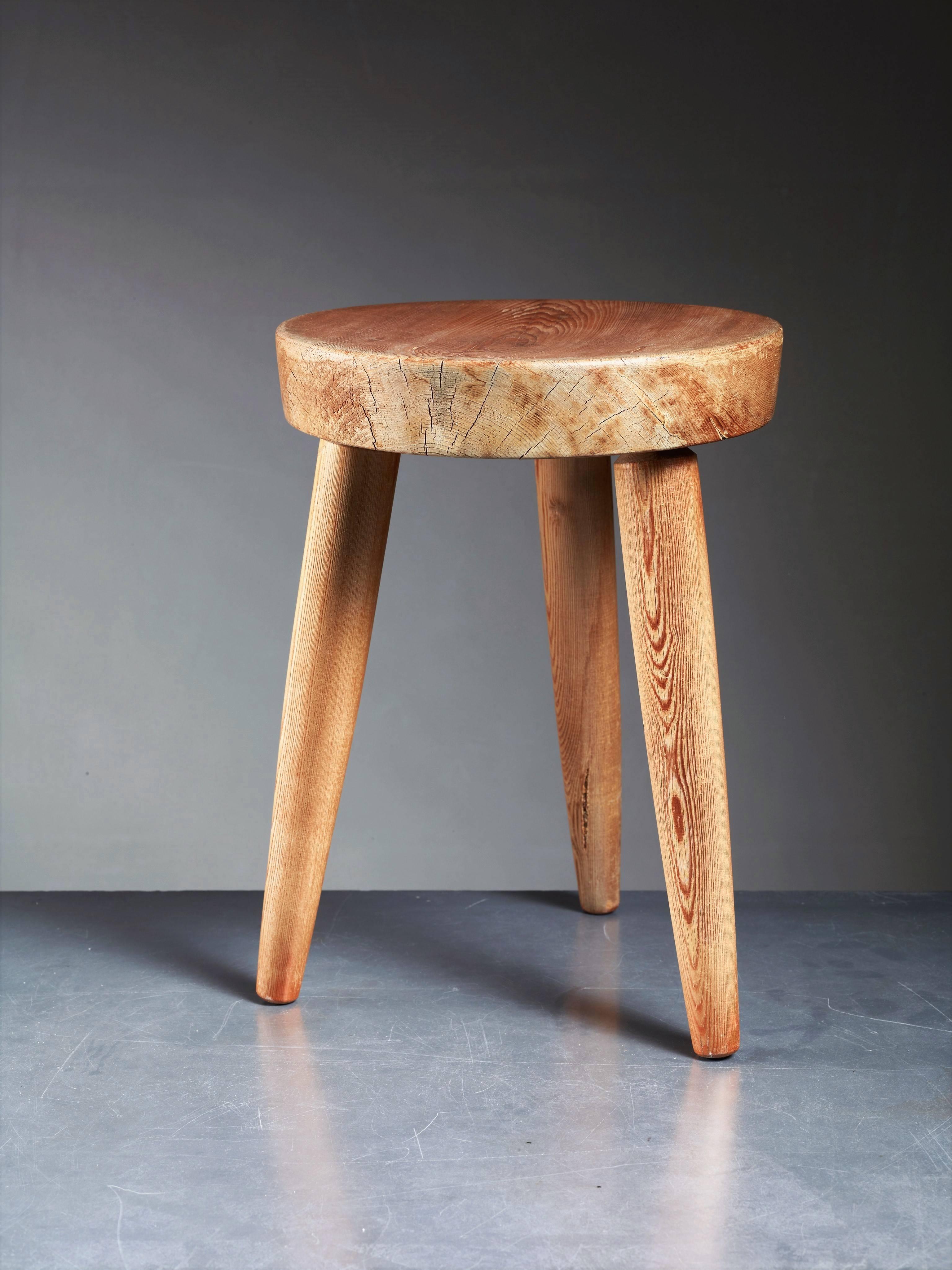 A rare pine tripod stool with a slightly concave seat and tapering legs by Charlotte Perriand. The wood has a beautiful and heavy patina.